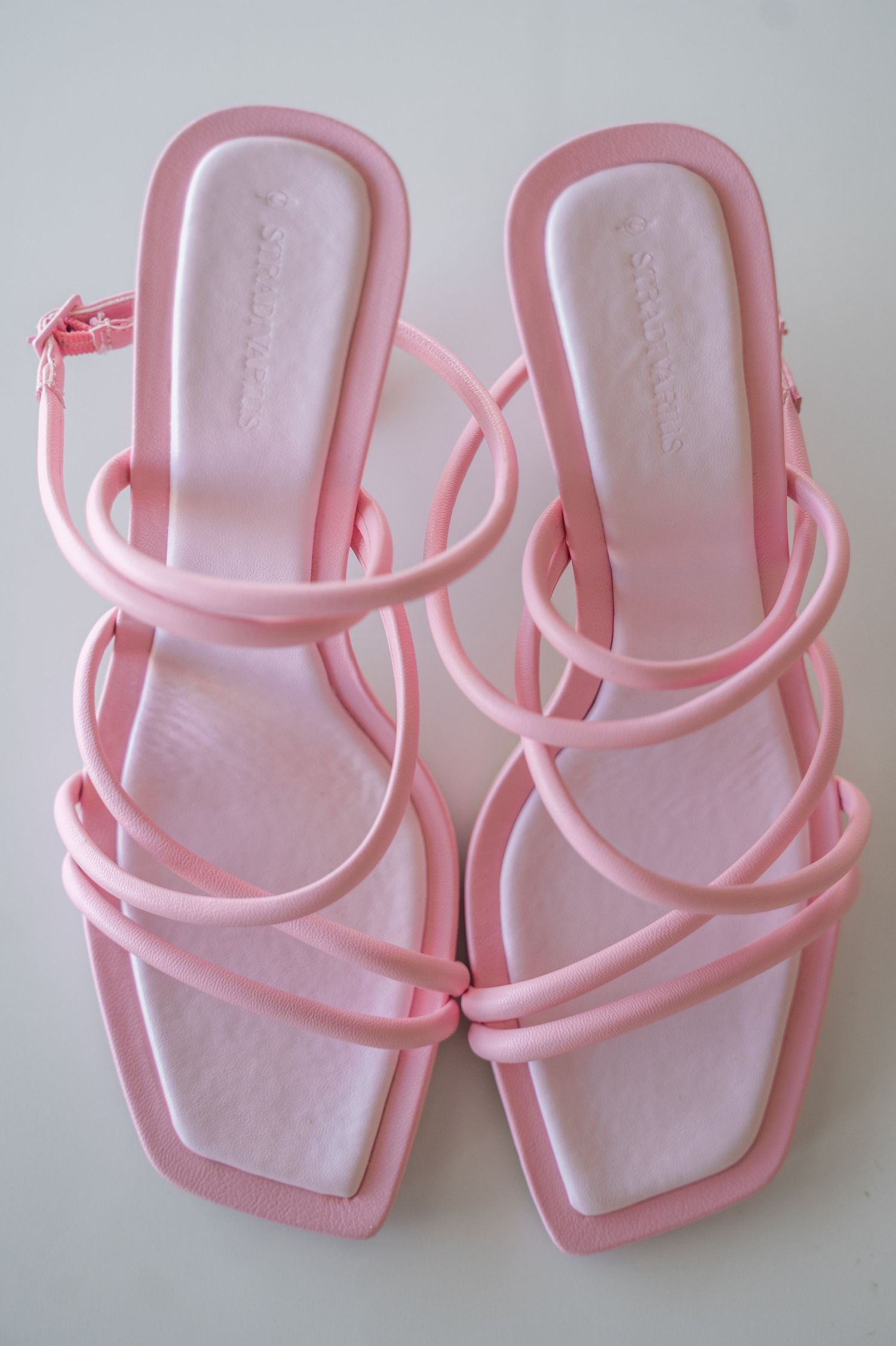 Four identical pairs of light pink plastic sandals with strappy details arranged in a row.