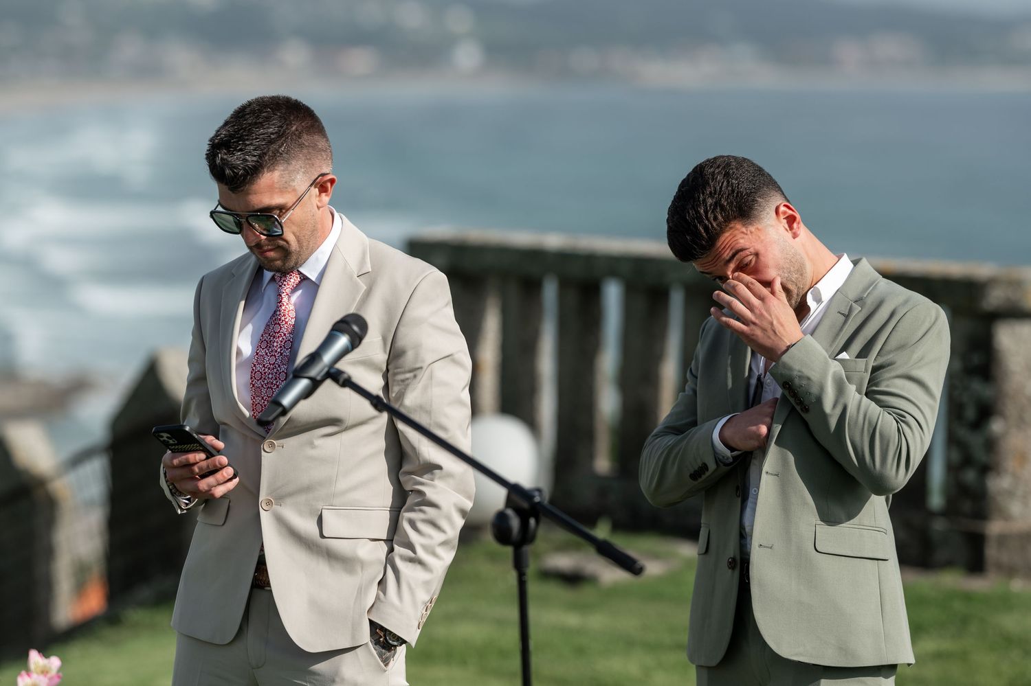 A person in a light gray suit wipes their face with a handkerchief during an emotional outdoor ceremony.
