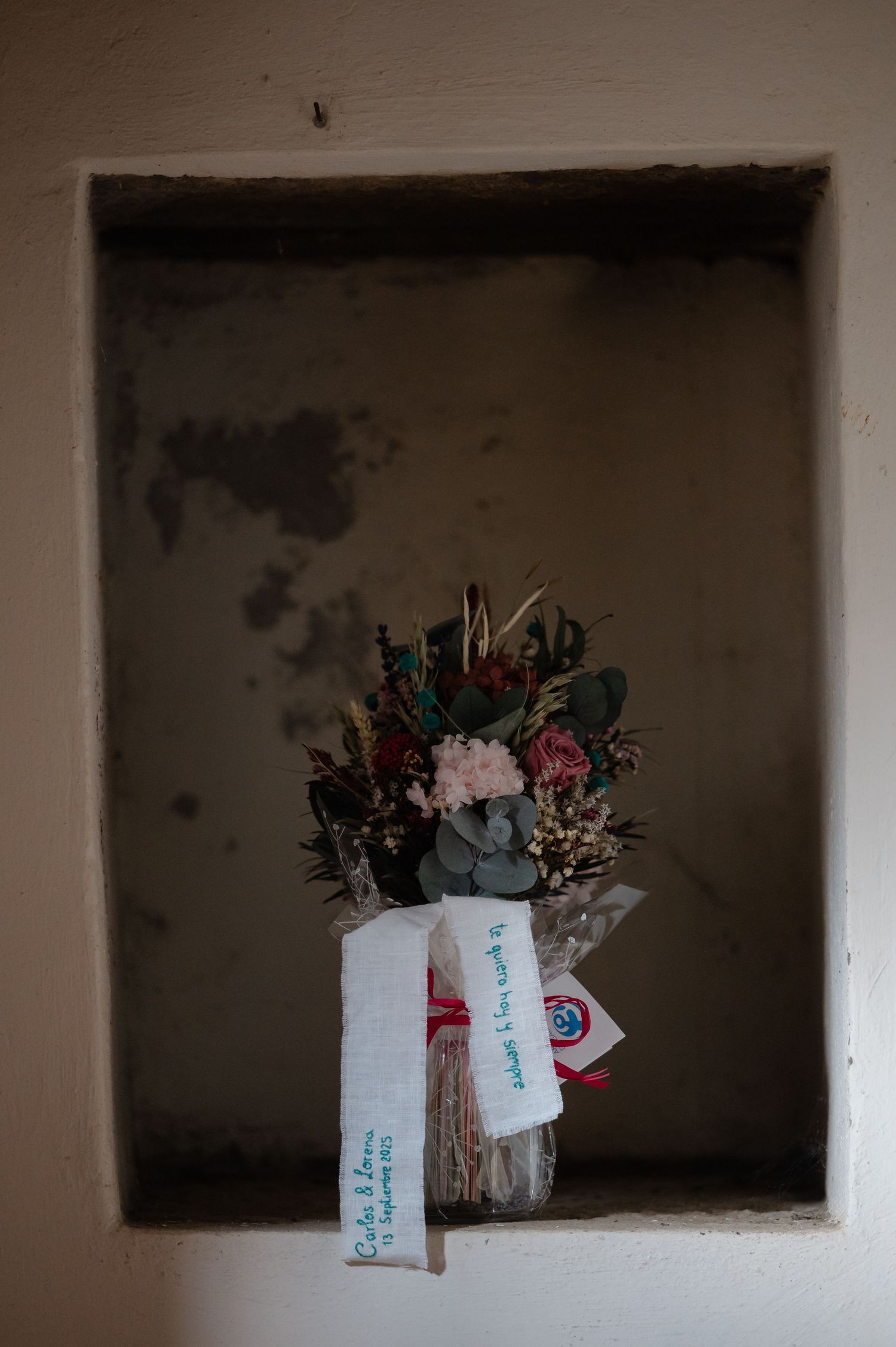 A series of dark wall niches displaying dried flower arrangements and small tags against a moody background.