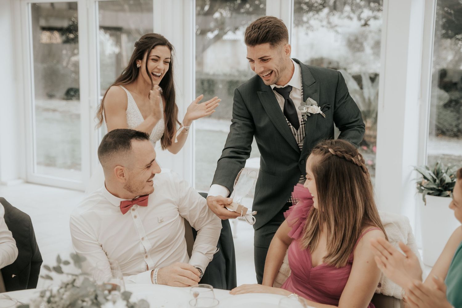 Wedding party members share joyful moments during outdoor celebration in natural light setting.
