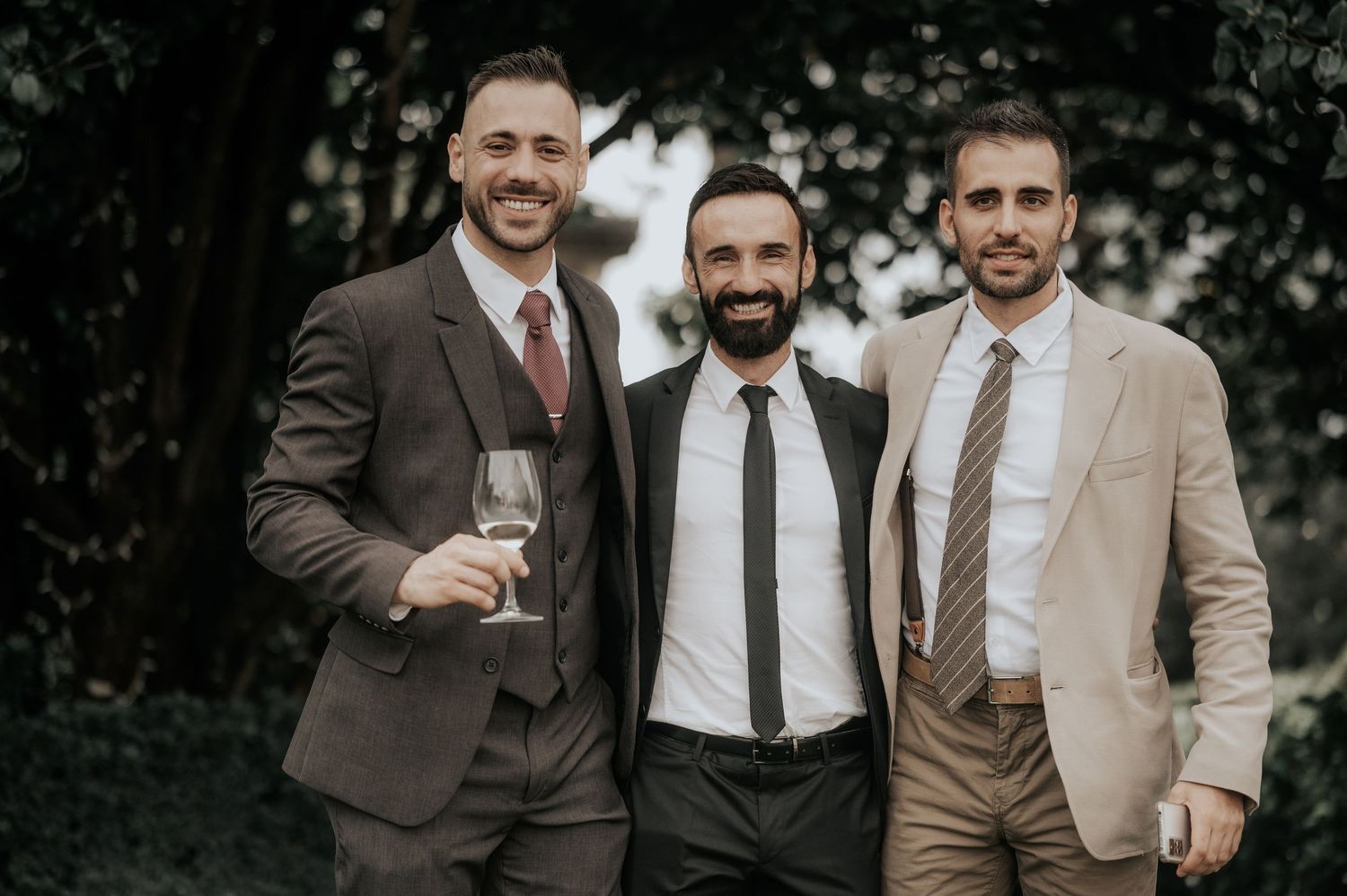 Groomsmen in suits smile and laugh together during outdoor wedding photos.