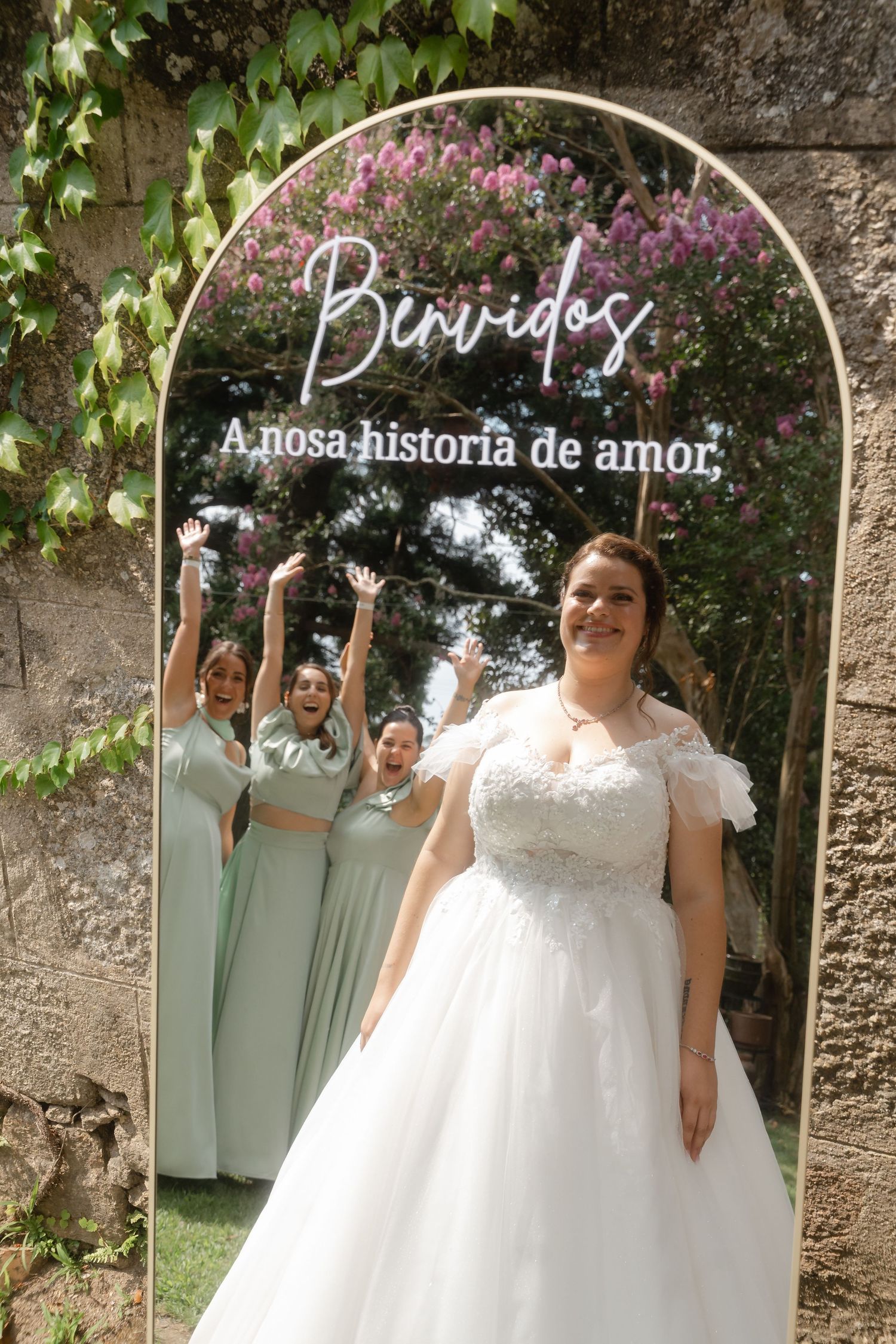 A wedding celebration in a garden setting with bridesmaids in sage green dresses and a bride in a white lace gown.
