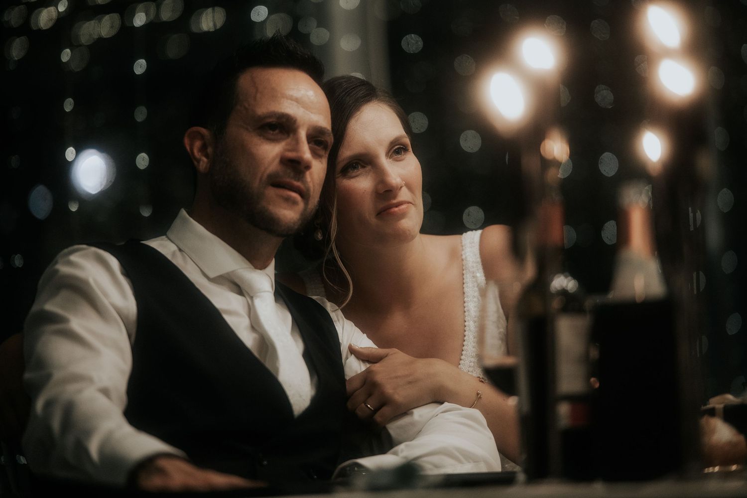 A couple shares an intimate dance moment at a wedding reception with soft glowing lights in the background.