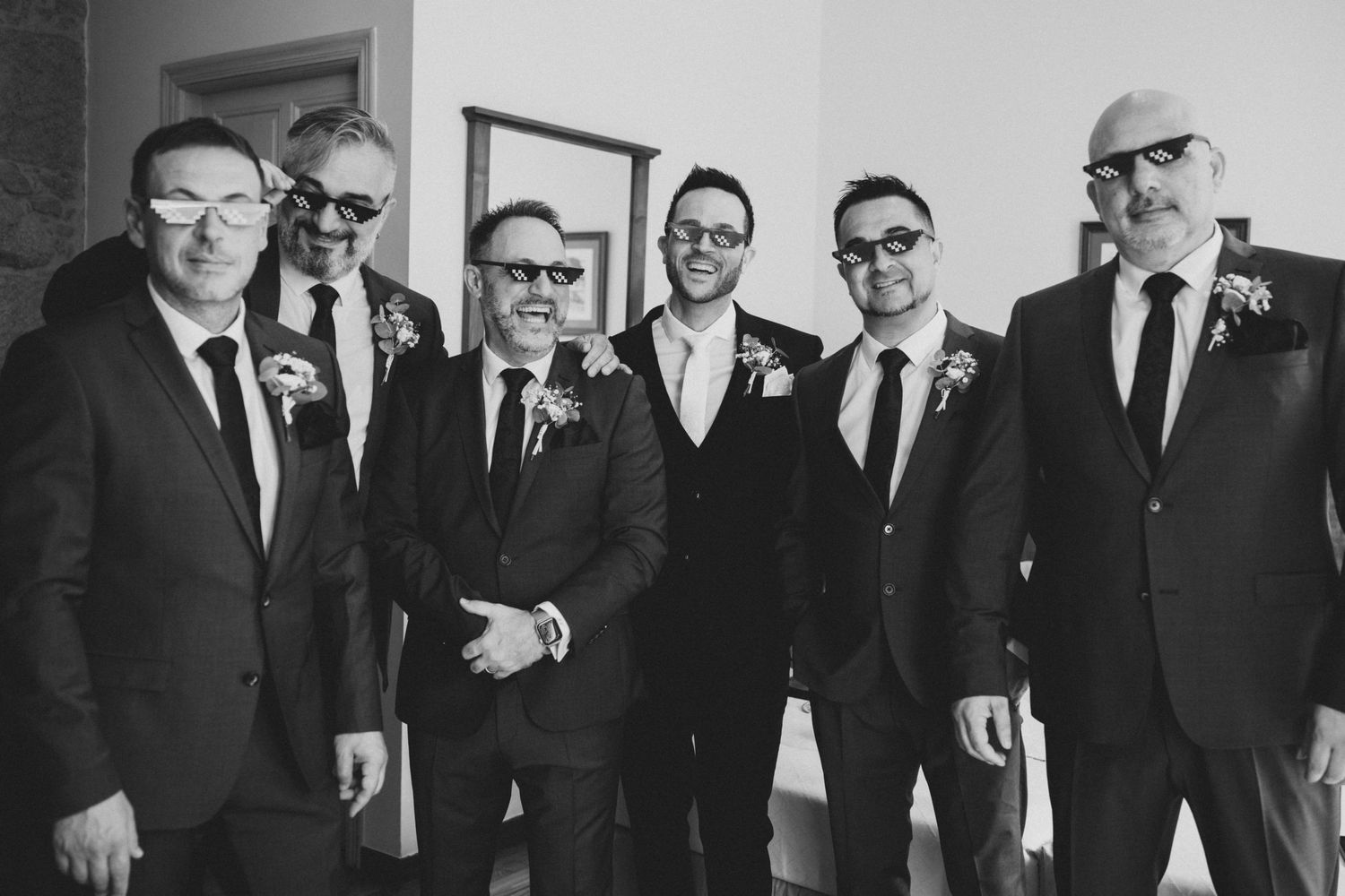 A black and white photo of groomsmen in dark suits and sunglasses posing together at a wedding.