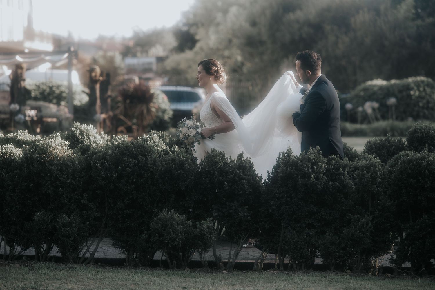 A panoramic wedding scene captured in moody lighting with trees and architecture in the background.