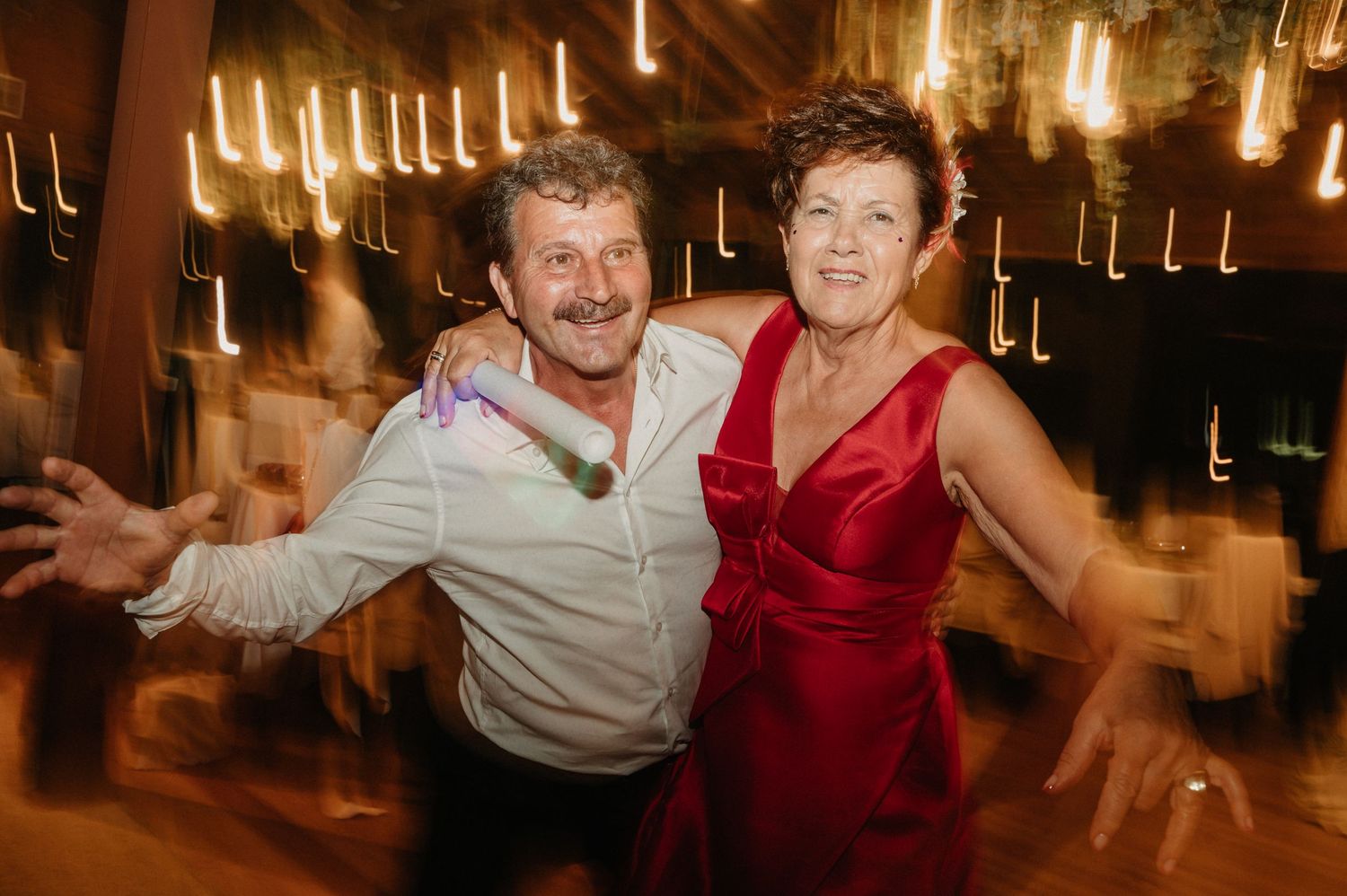 Energetic couple dancing together at a reception venue with warm glowing lights in the background.