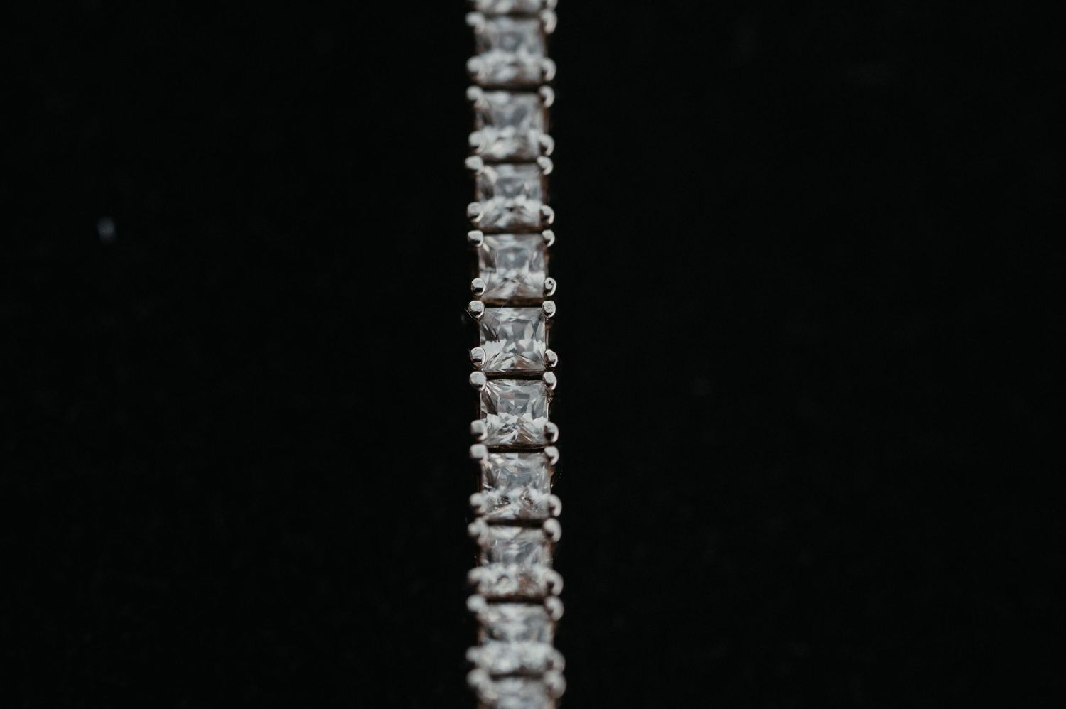 A silver rhinestone necklace or bracelet strand sparkles against a black background.