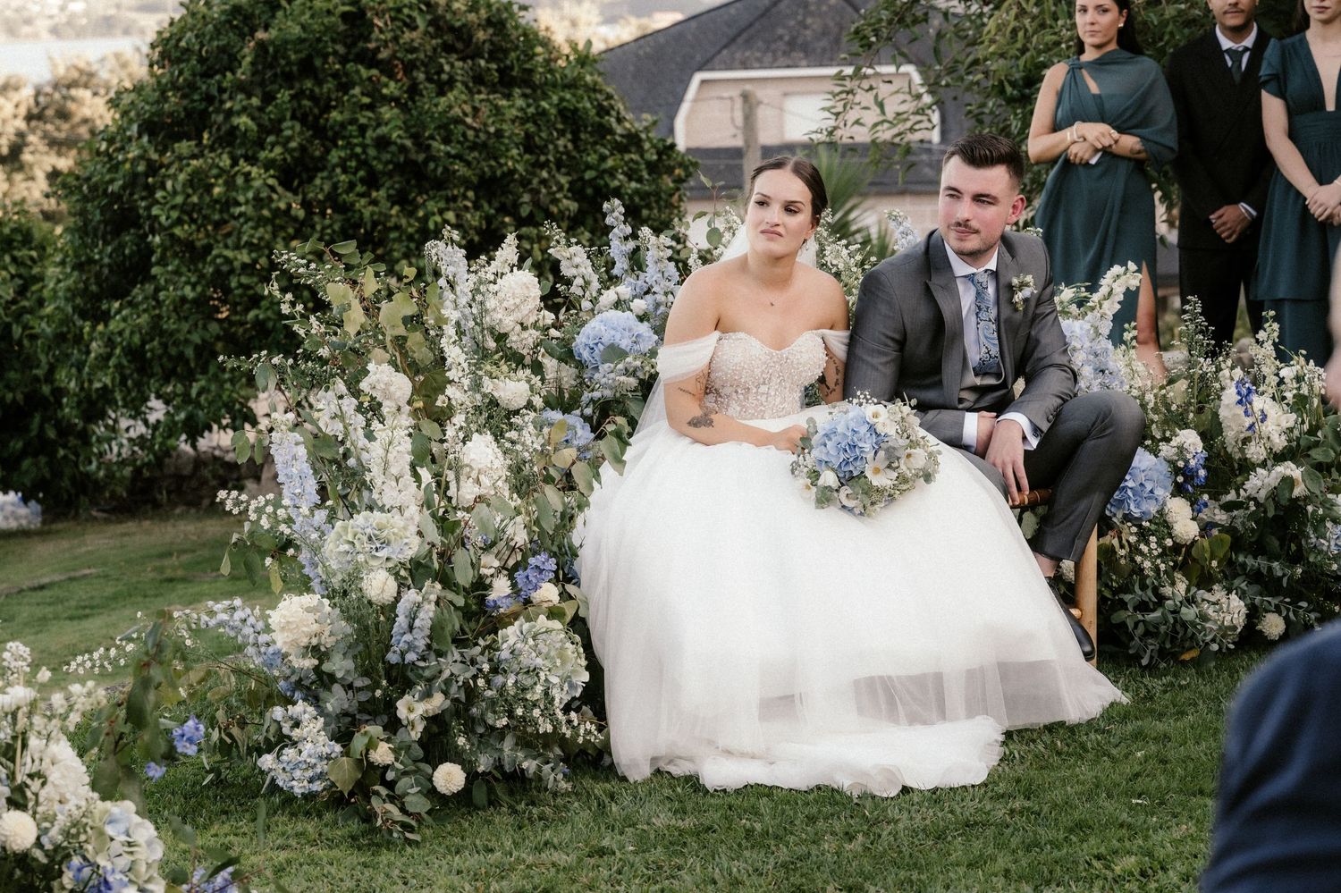 A couple shares a romantic moment in a garden surrounded by white floral arrangements during their wedding celebration.