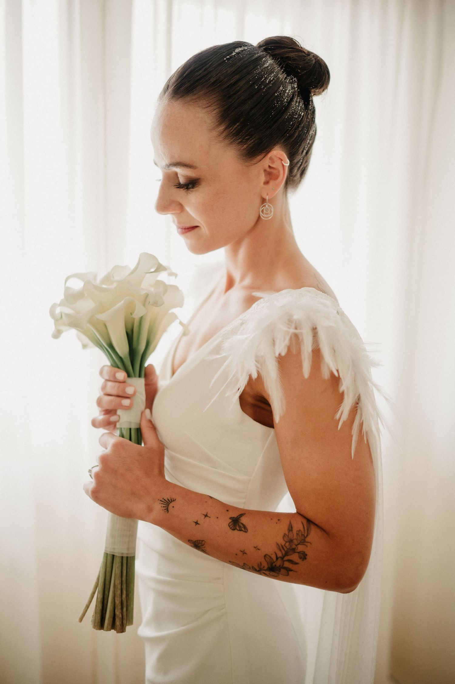 Elegant bridal portrait with white calla lily bouquet and feather-adorned wedding gown.