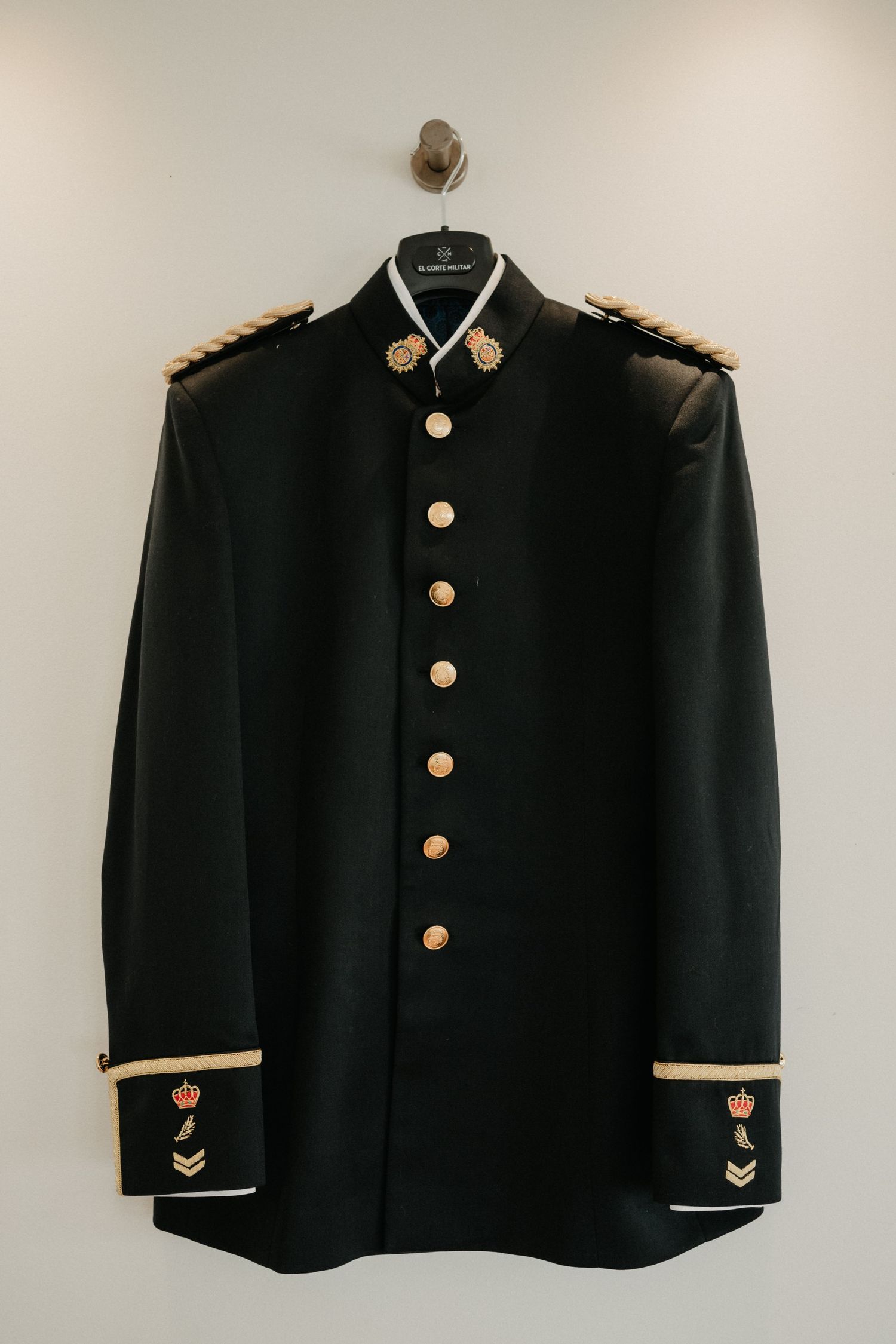 Black vintage military uniform jacket with gold buttons and collar details displayed on hangers against white background.