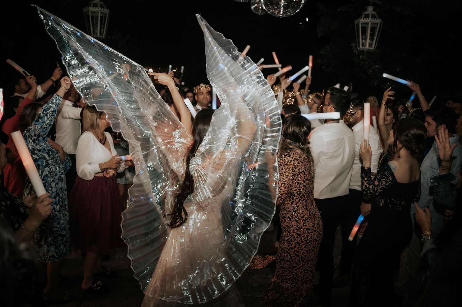 People dancing and celebrating at a wedding reception with glowing lights and sparklers creating a festive atmosphere.