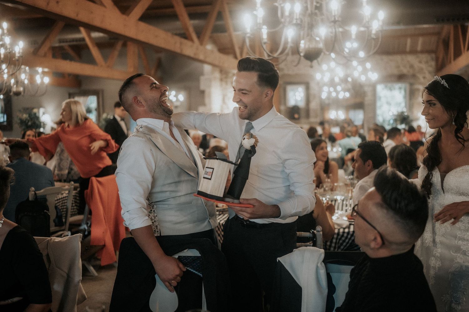 Wedding reception party with chandeliers and exposed wooden beams creating an intimate atmosphere.