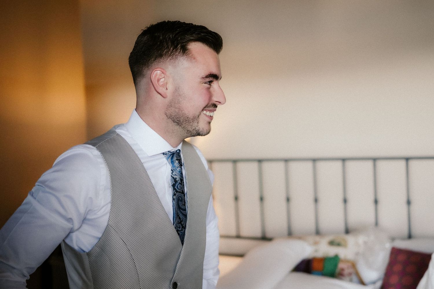 A groom in a light gray suit and blue tie poses during formal wedding photos.