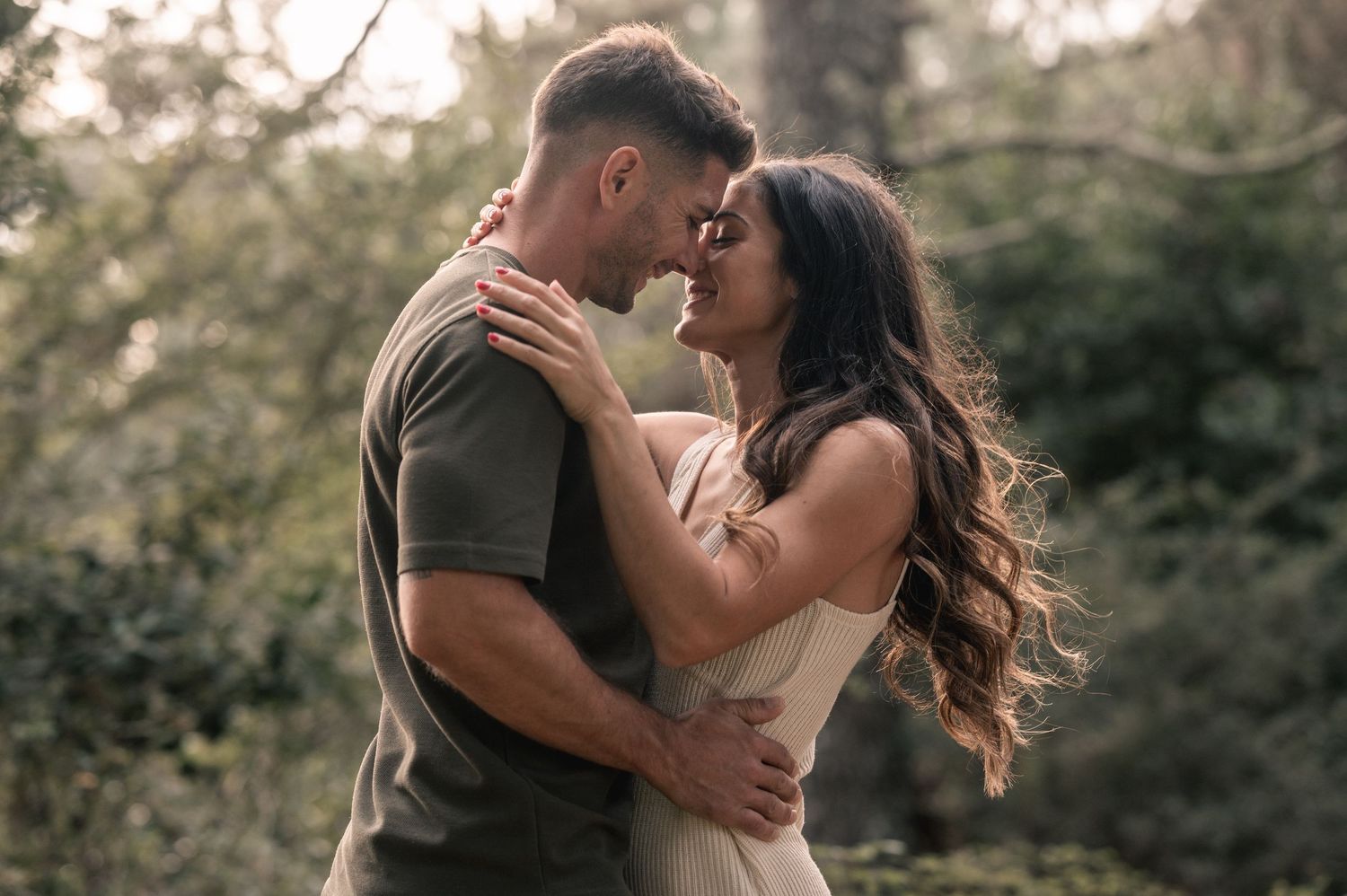 A romantic couple embraces outdoors during golden hour in a natural setting.