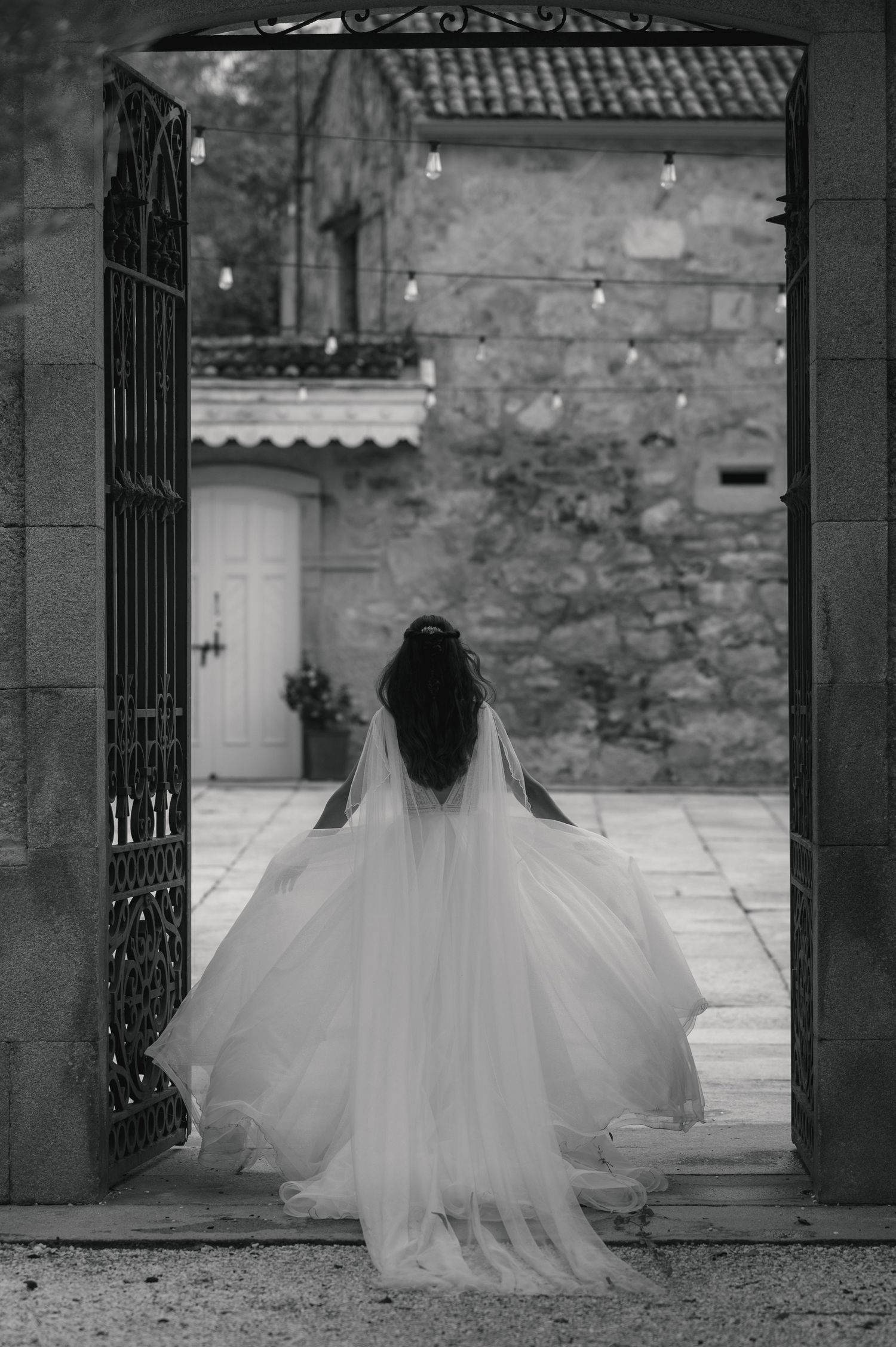 Black and white photos show a bride in a flowing gown and veil standing in a stone courtyard.