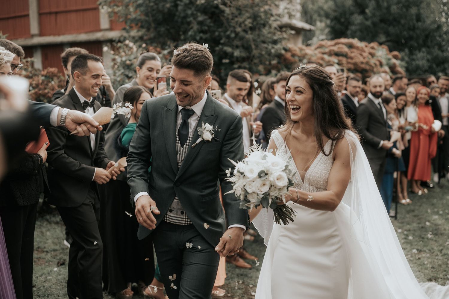 Joyful wedding celebration outdoors with guests gathering on a lawn near brick buildings.