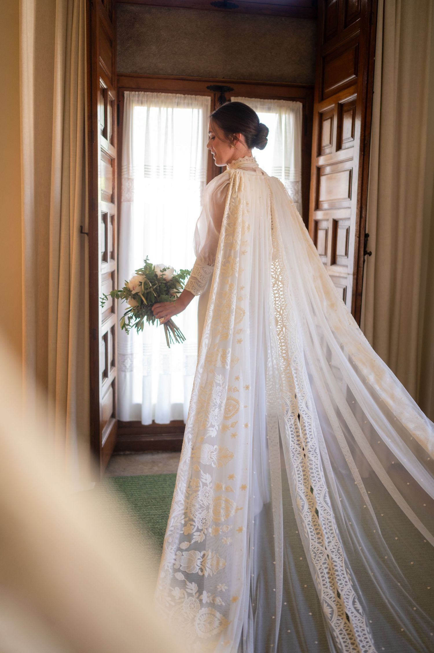 A flowing white wedding veil with delicate lace details hangs elegantly in a sunlit hallway.