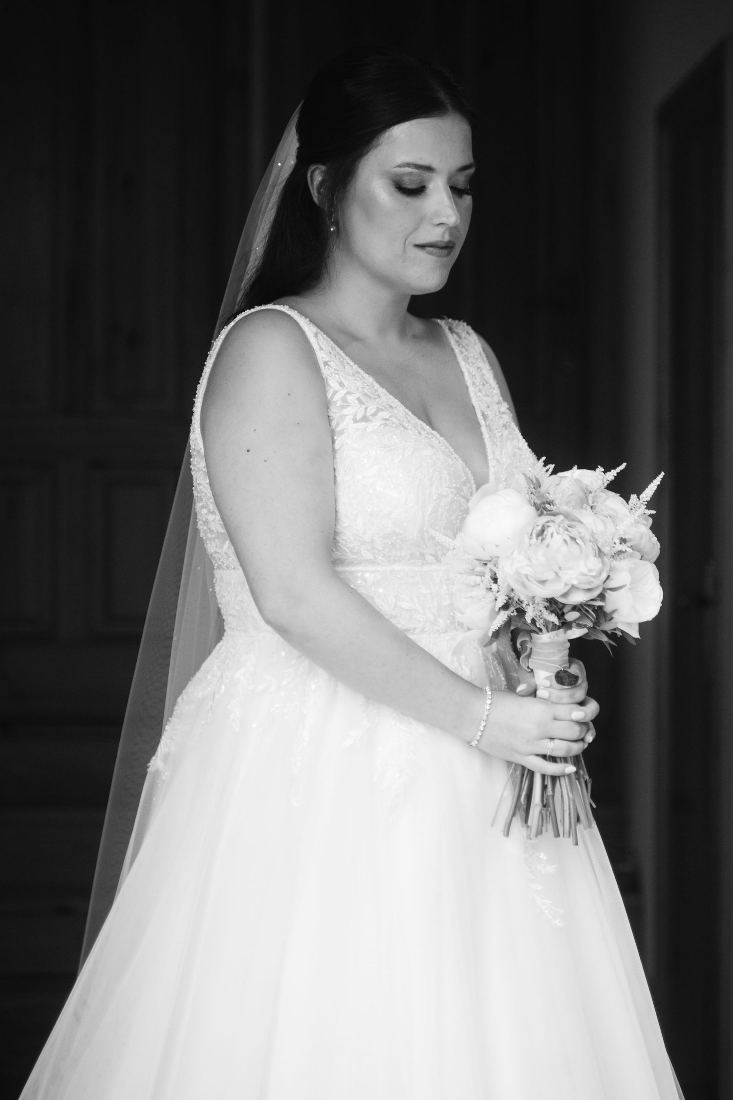 Black and white photo of a bride in a lace wedding dress holding a white floral bouquet.