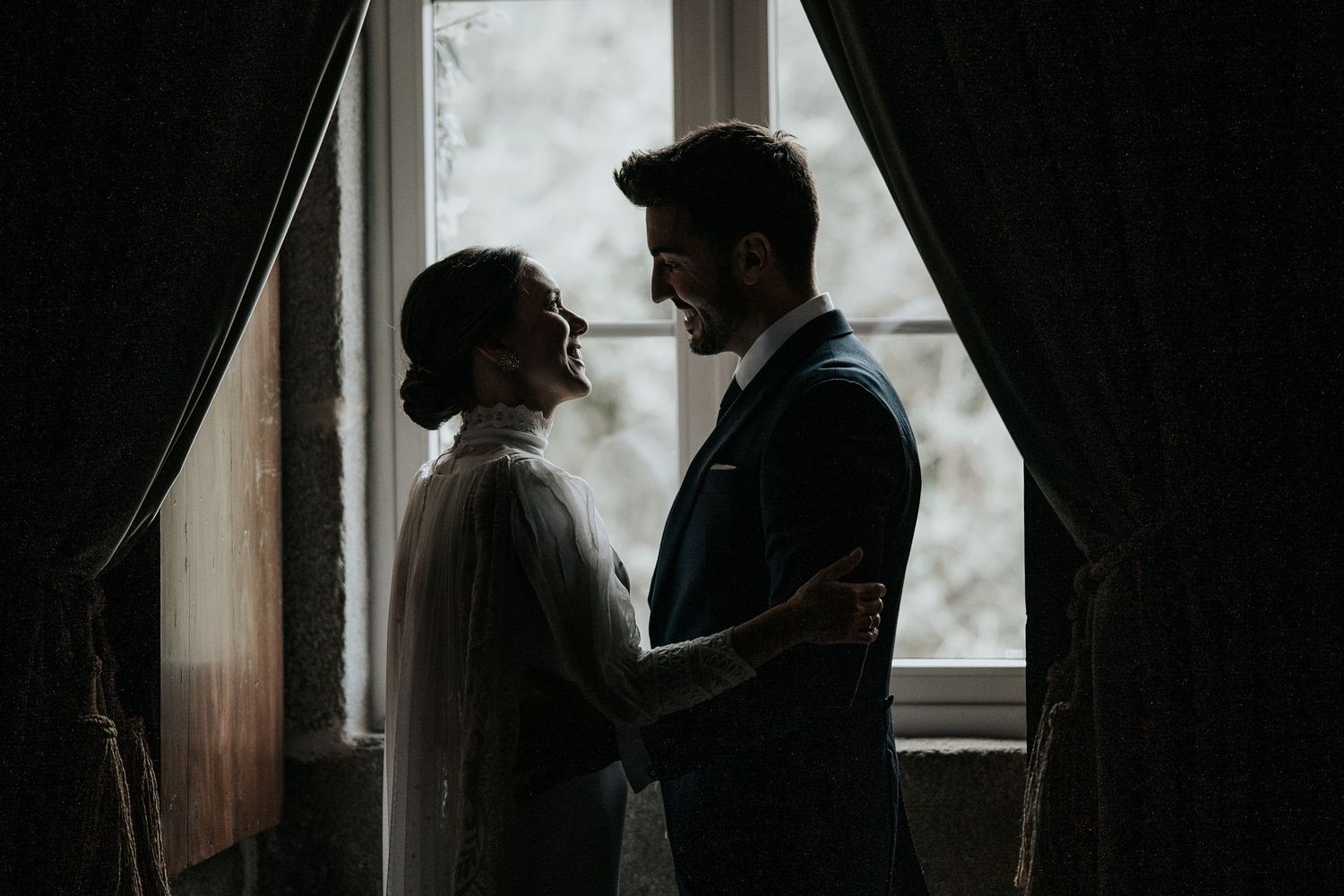 Silhouetted couple standing by window in dark moody lighting creating romantic atmosphere.