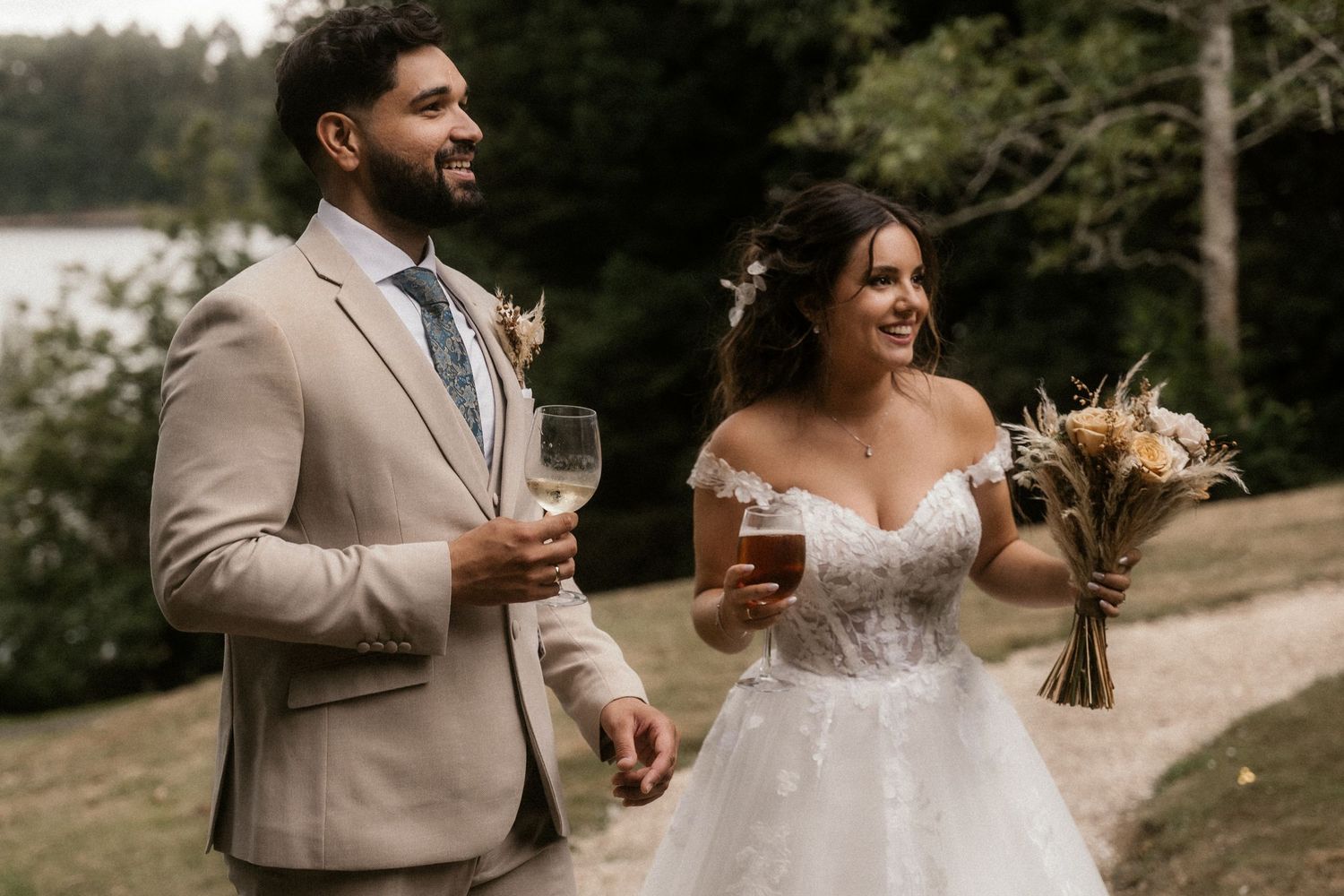 A couple shares a joyful moment with wine glasses during an outdoor wedding celebration in natural surroundings.
