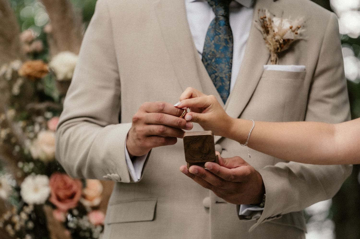Close-up shot of hands exchanging wedding rings during an outdoor ceremony.