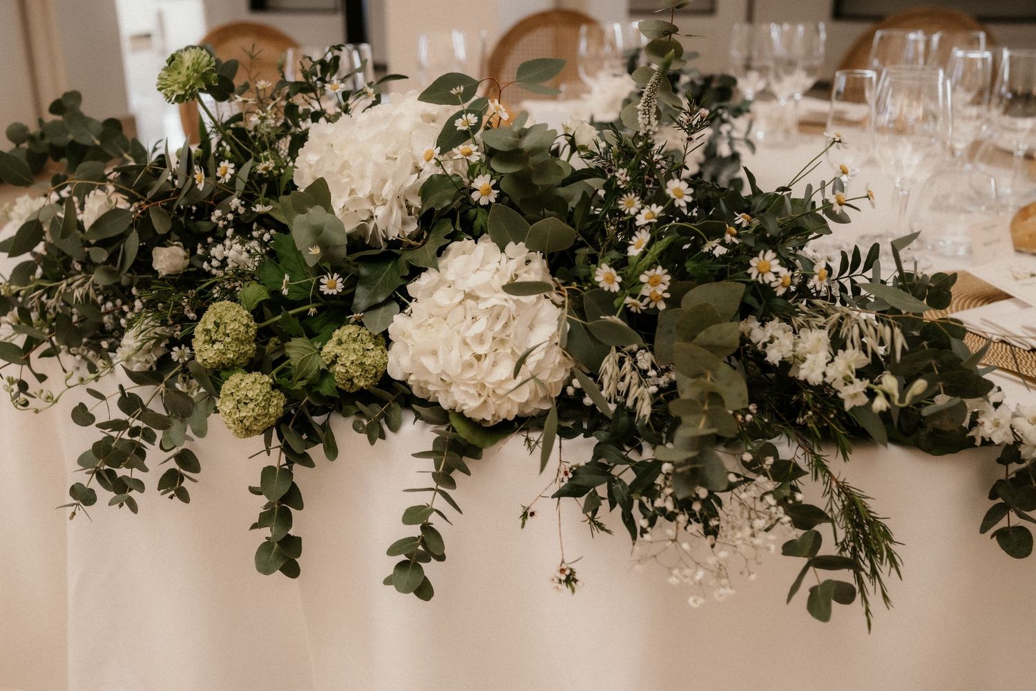 Elegant wedding reception table decorated with lush white roses and greenery garlands along with crystal glassware.