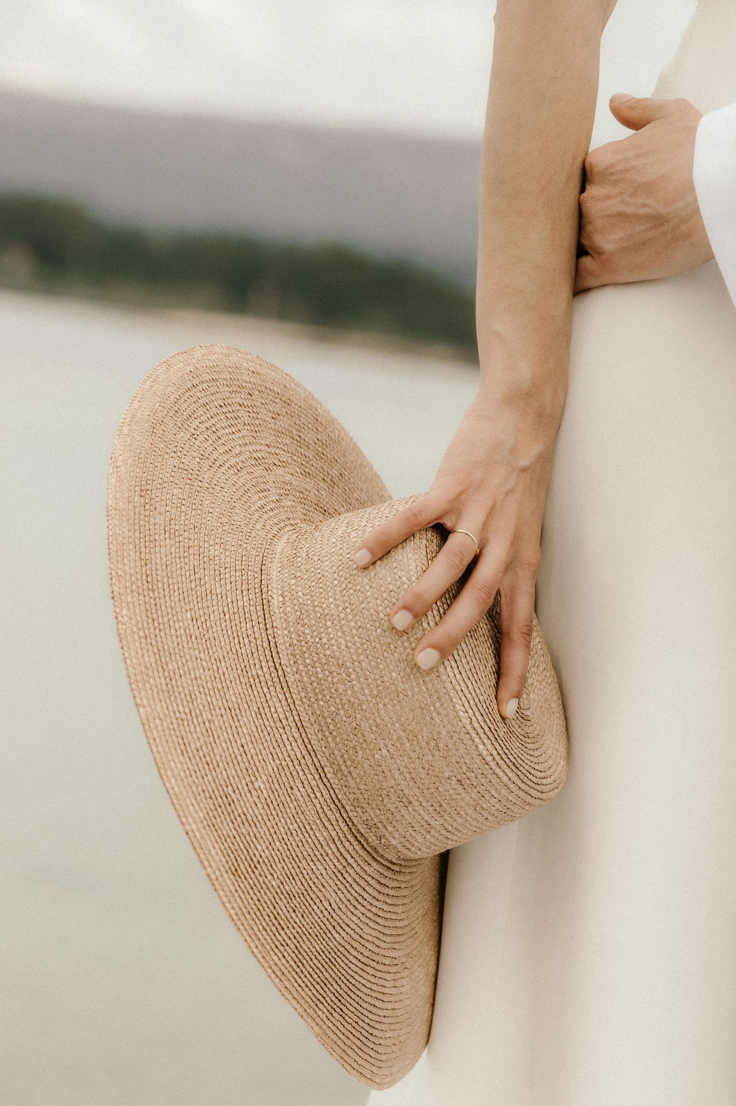 Close-up view of hands holding a beige straw sunhat against a blurred outdoor background.