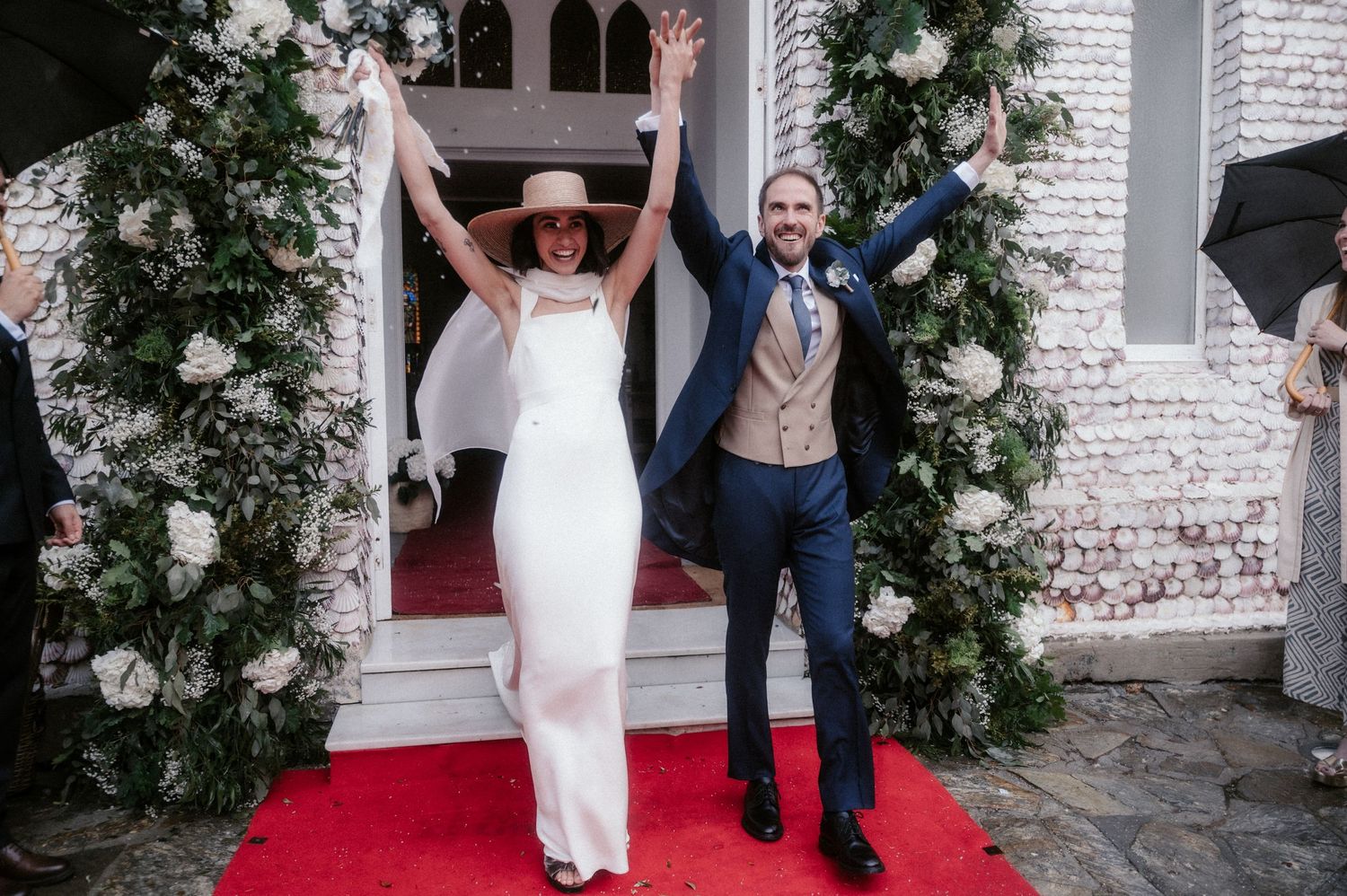 Newlyweds walk down a white brick church aisle decorated with evergreen garlands.