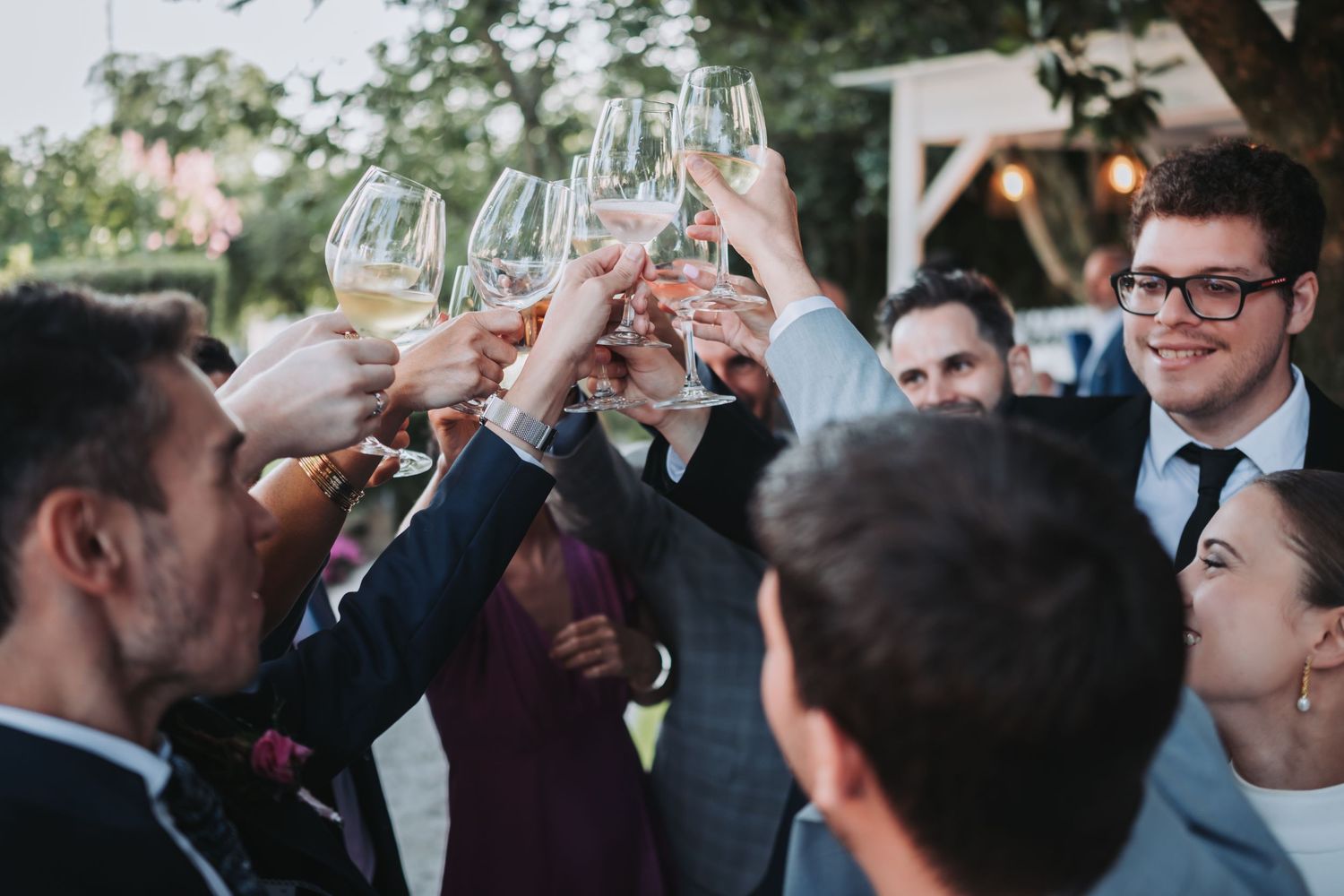 Wedding guests raise champagne glasses in a celebratory toast during an outdoor reception.
