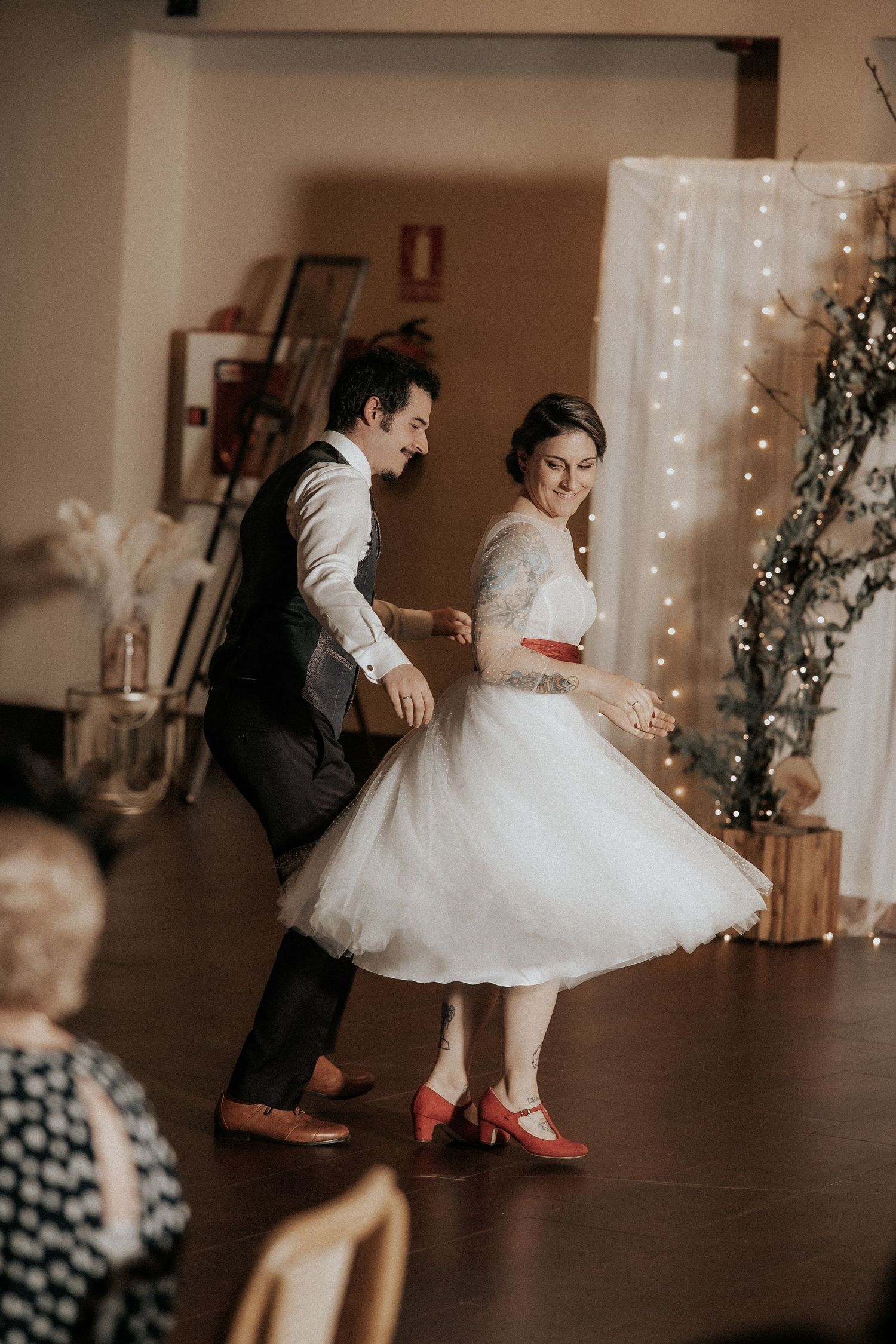 A couple dances together in a romantic moment with twinkle lights in the background.