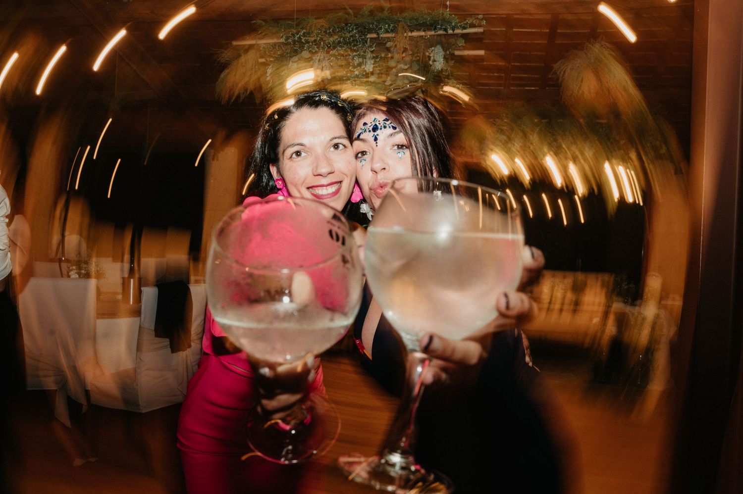 Two friends enjoy large cocktails at a party with motion blur and tunnel lighting effects in the background.