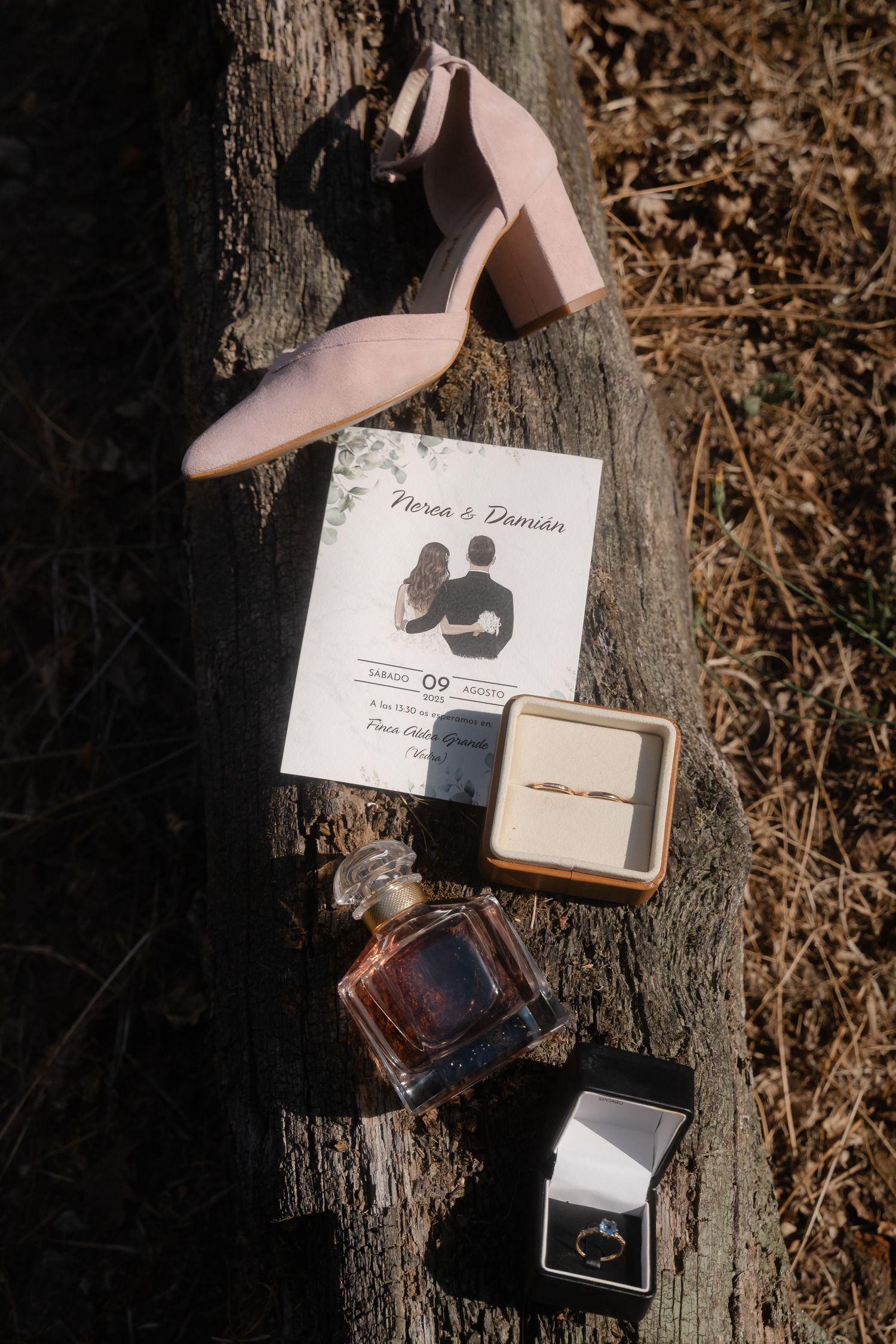 Wedding details including rings, invitation and perfume bottle arranged artistically on rustic wood surface.