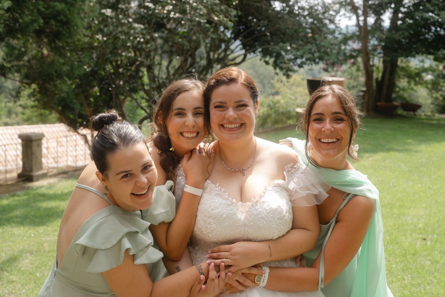 A group wearing pastel dresses and formal attire poses outdoors for candid photos in a garden setting.
