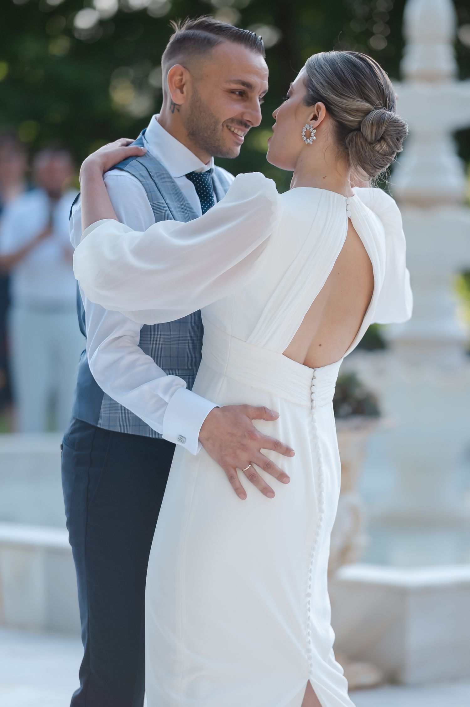 A romantic moment between newlyweds dancing, with the bride in a white backless dress and groom in a gray vest.