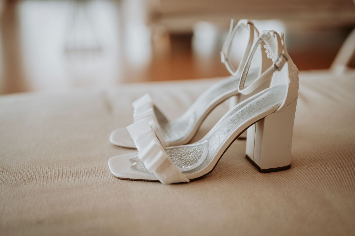 Multiple views of white bridal sandals with chunky heels arranged in a row on a wooden surface.
