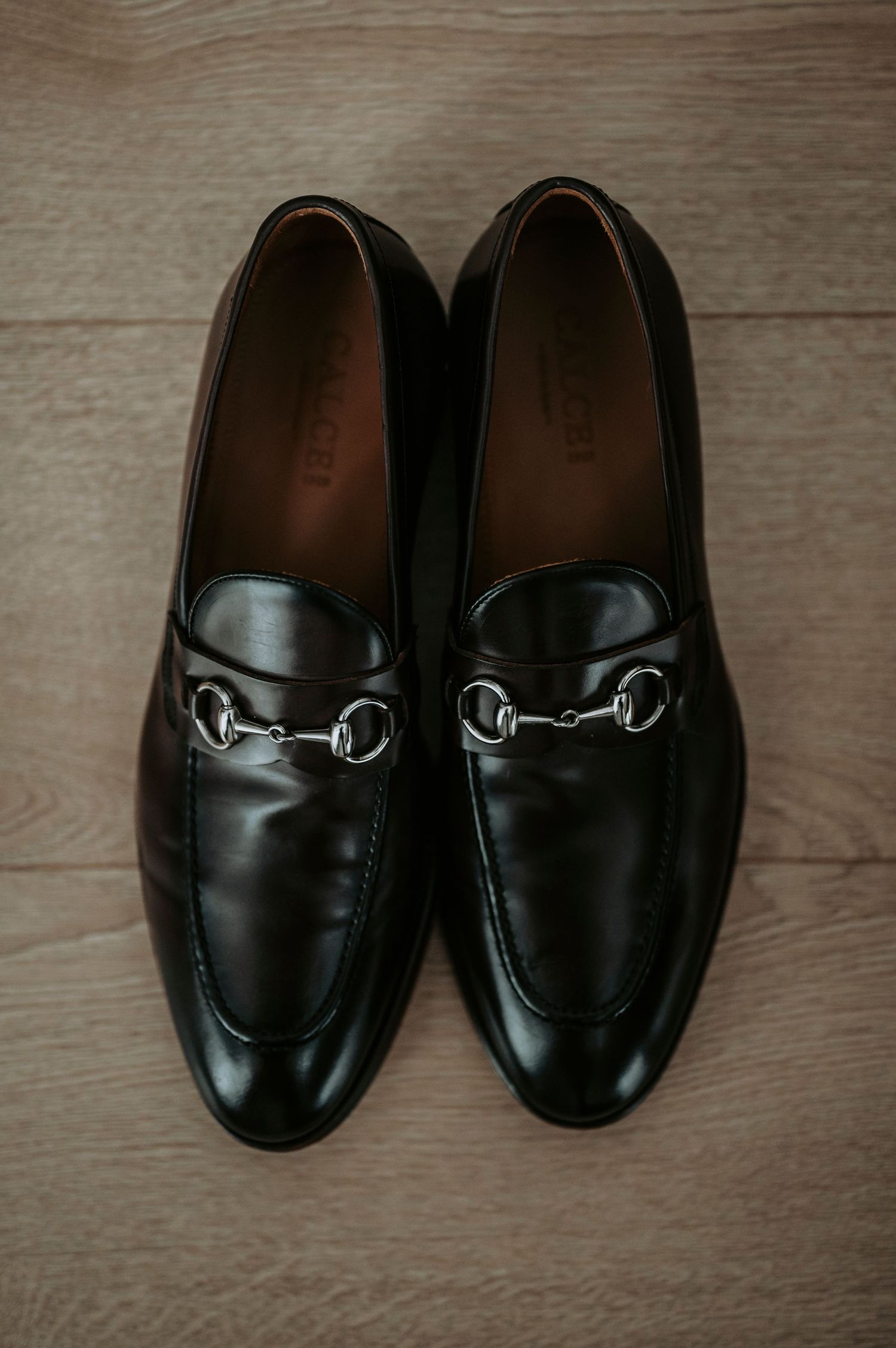 Black leather Gucci horsebit loafers arranged in a row showing different angles on wooden floor.