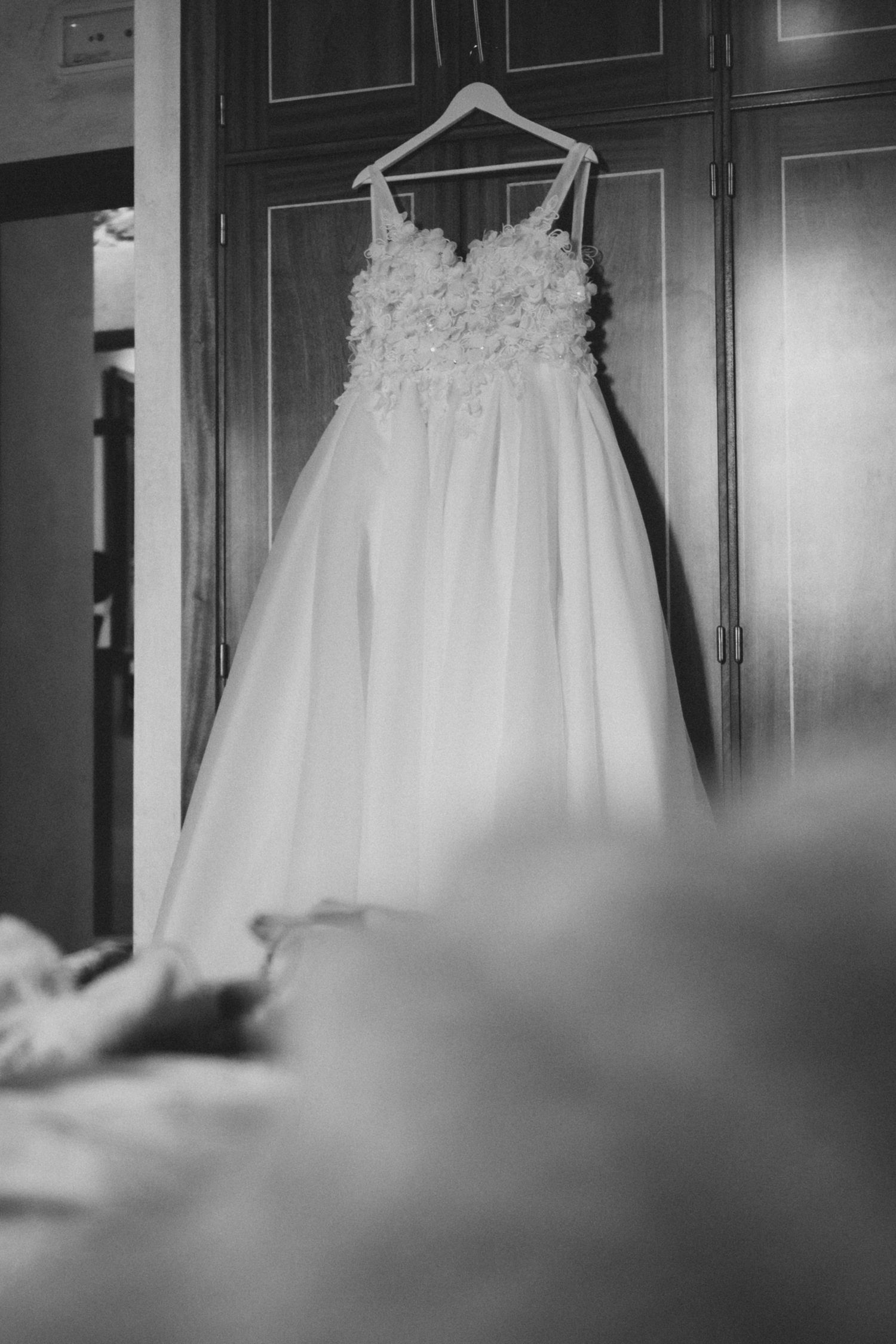 Black and white photo series showing a delicate white dress hanging on a hanger against a dark wall.