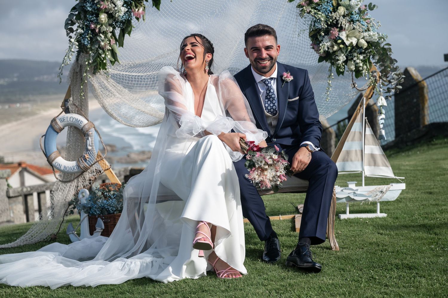 Newlyweds sharing a playful moment on grassy lawn under decorative floral arrangements.