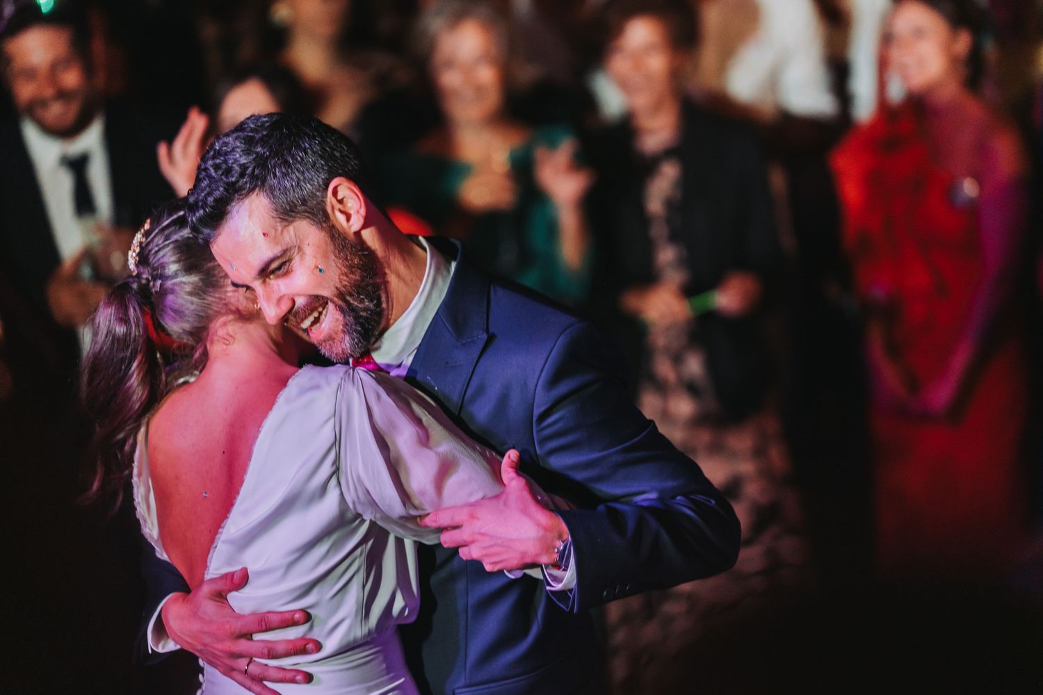 A couple shares an intimate dance moment at a wedding reception with guests visible in the background.