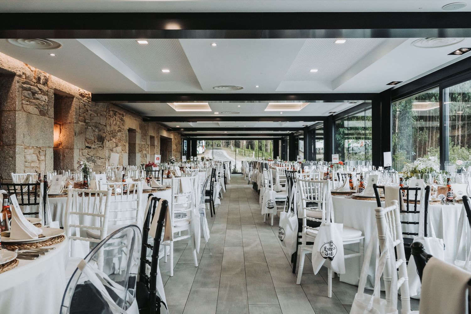 Elegant wedding reception venue with white tables, black chairs, and stone accent walls in a modern indoor setting.