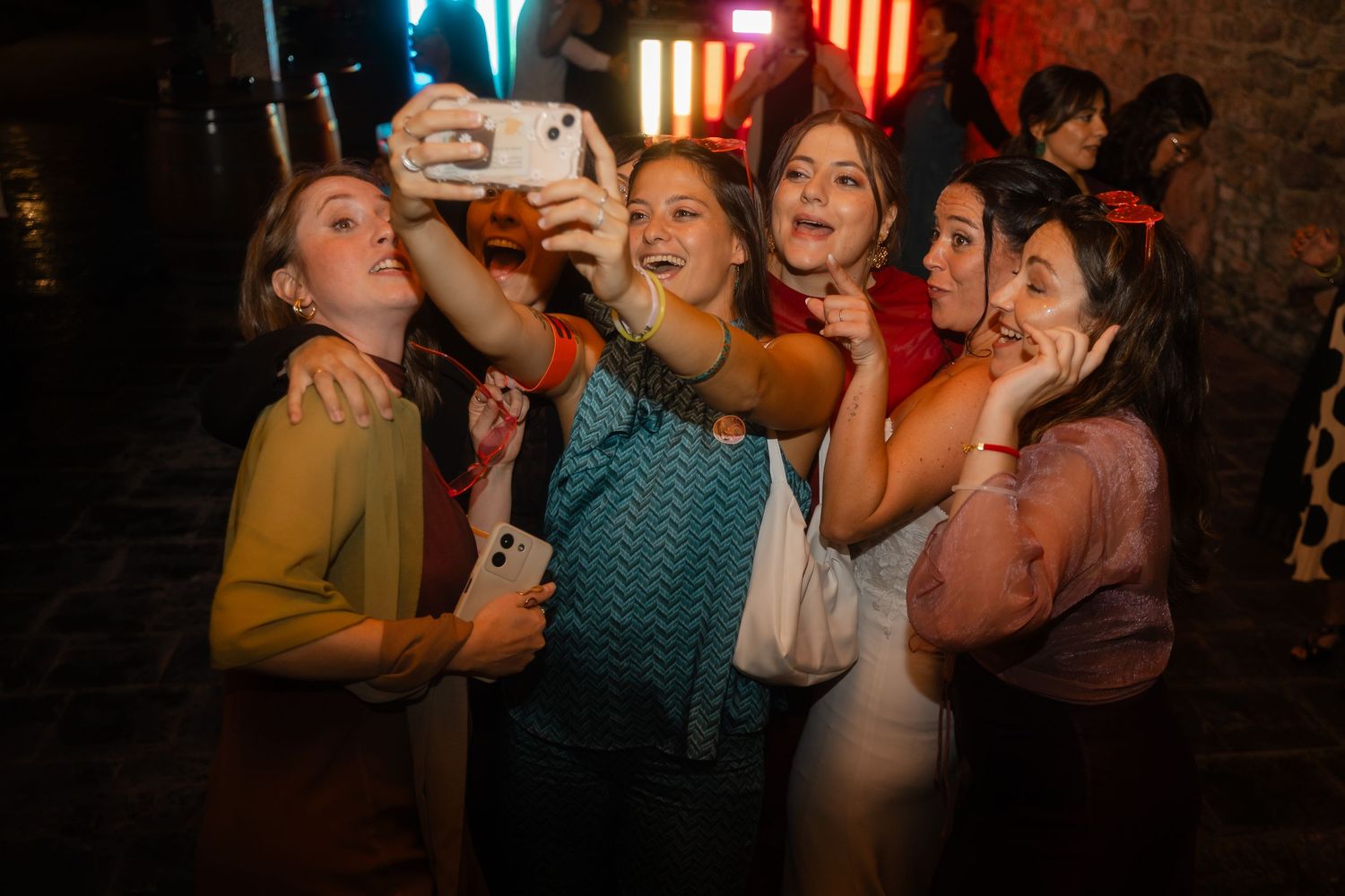 Group of friends laughing and dancing together at a dimly lit party venue.