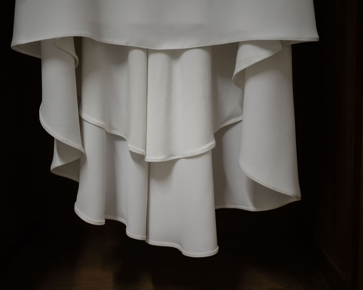 White flowing fabric with delicate draping and soft folds against a dark background.