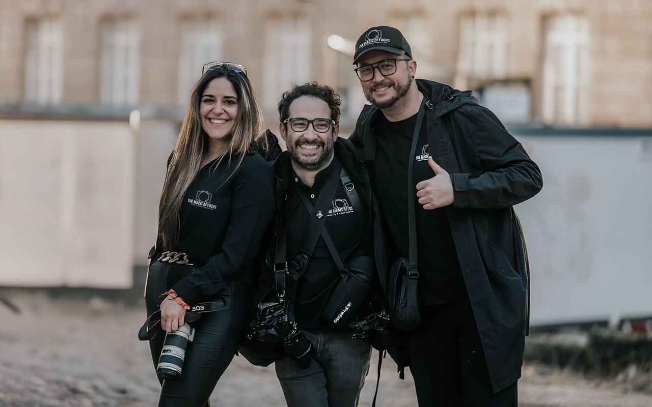 A group of photographers in black clothing smile and laugh together while holding professional cameras outdoors.