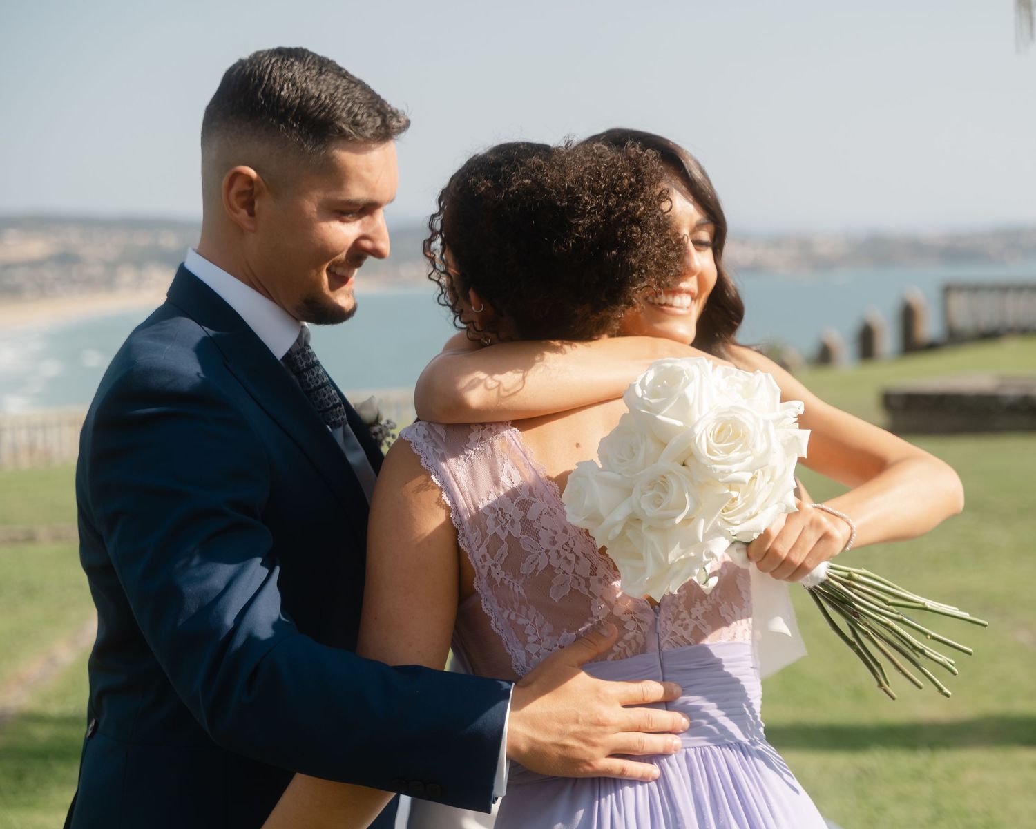 Couple embraces while holding white bouquet during outdoor wedding photoshoot.