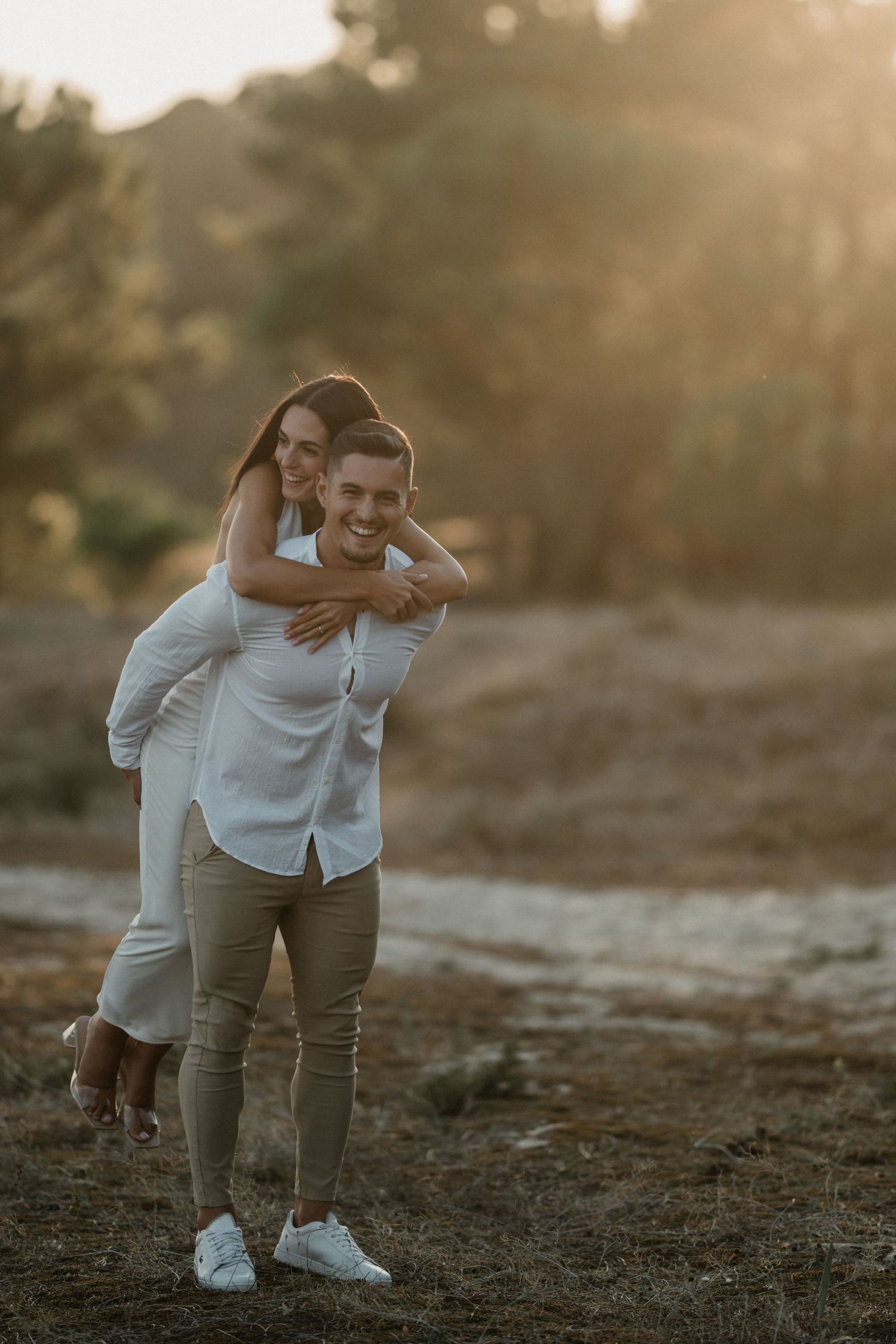A joyful couple laughs together during their outdoor photo session in golden sunlight.