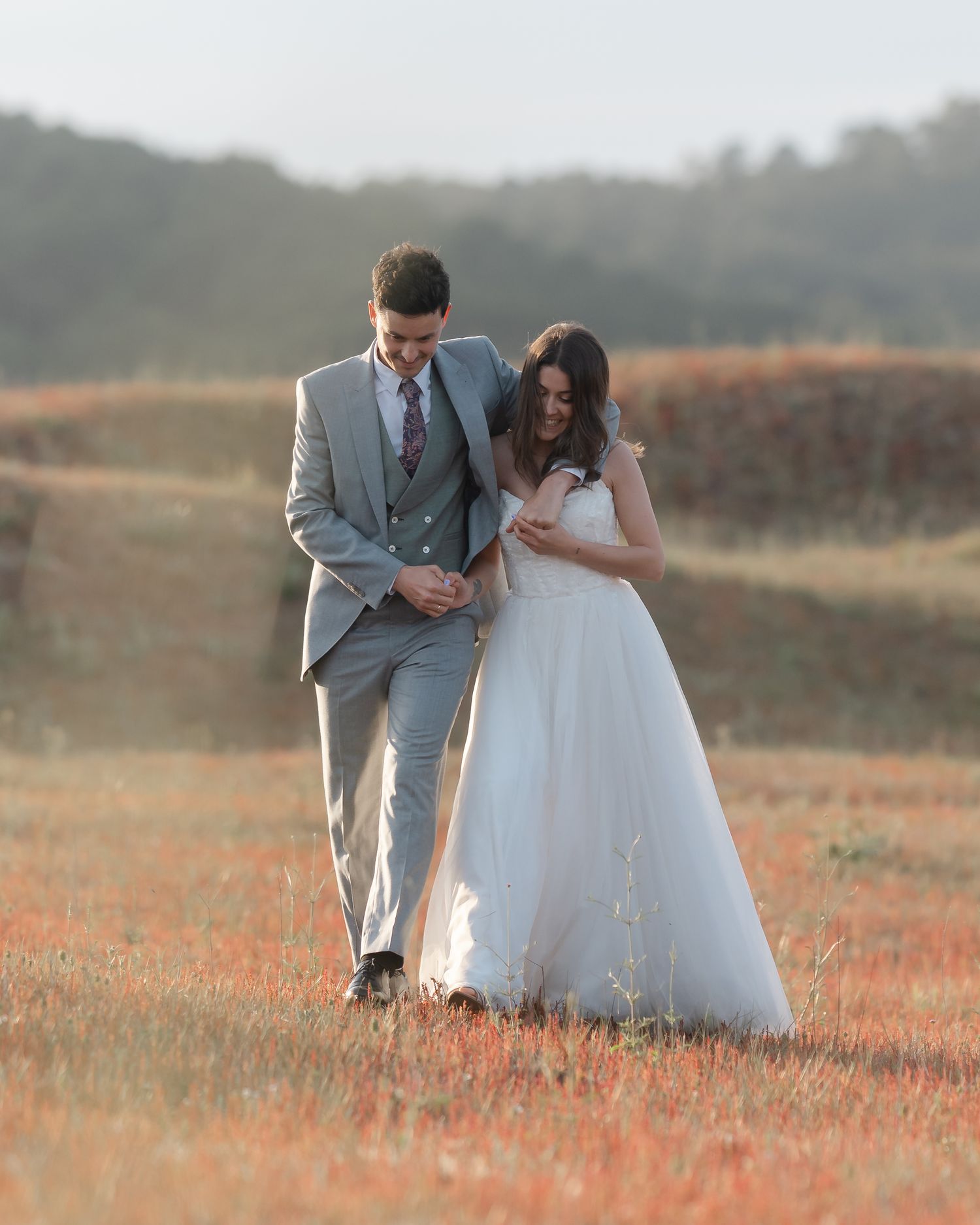 Bride and groom walking hand in hand through a golden wildflower field during sunset wedding photoshoot.