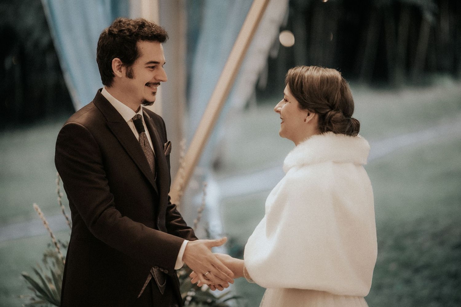 Couple in wedding attire sharing a tender moment outdoors with a soft, muted background.