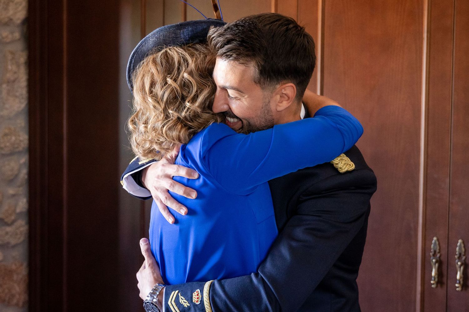 Two people embrace in a tender moment at a venue with wooden paneled walls.