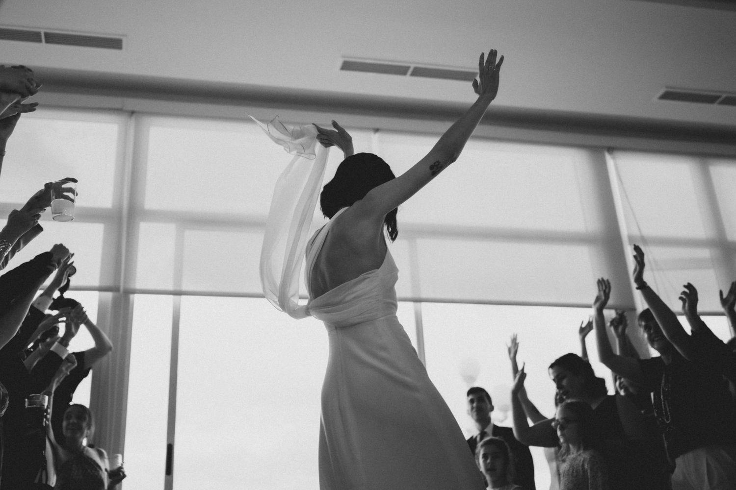 Silhouettes of people dancing with raised arms against bright windows in a party setting.