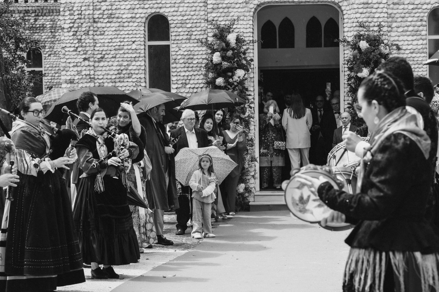 A vintage black and white photograph shows graduates in academic regalia lining a walkway outside a stone building.